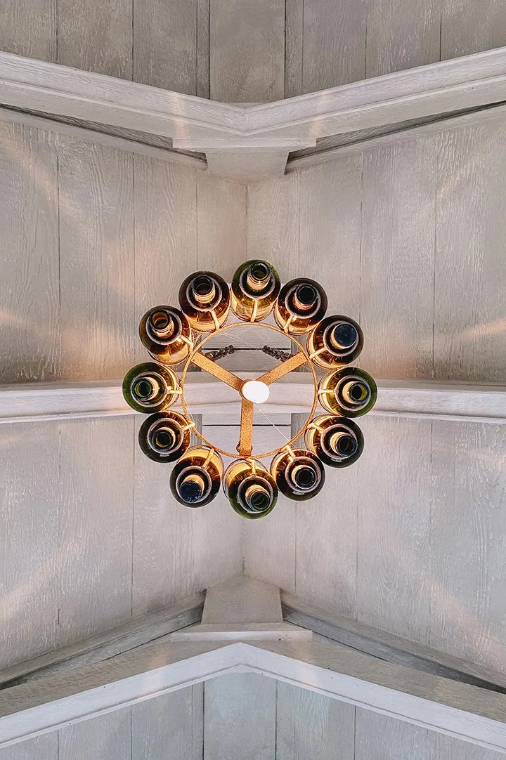 Vintage Edison bulb wine bottle chandelier inside Château de LuVi, adding warm ambient light and handcrafted character to the limewashed interior space.