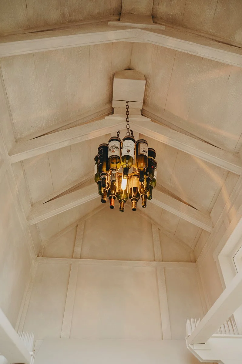 Exposed trusses and vintage Edison bulbs beneath a softly limewashed ceiling at Château de LuVi, creating warmth, texture, and a timeless artisan atmosphere.