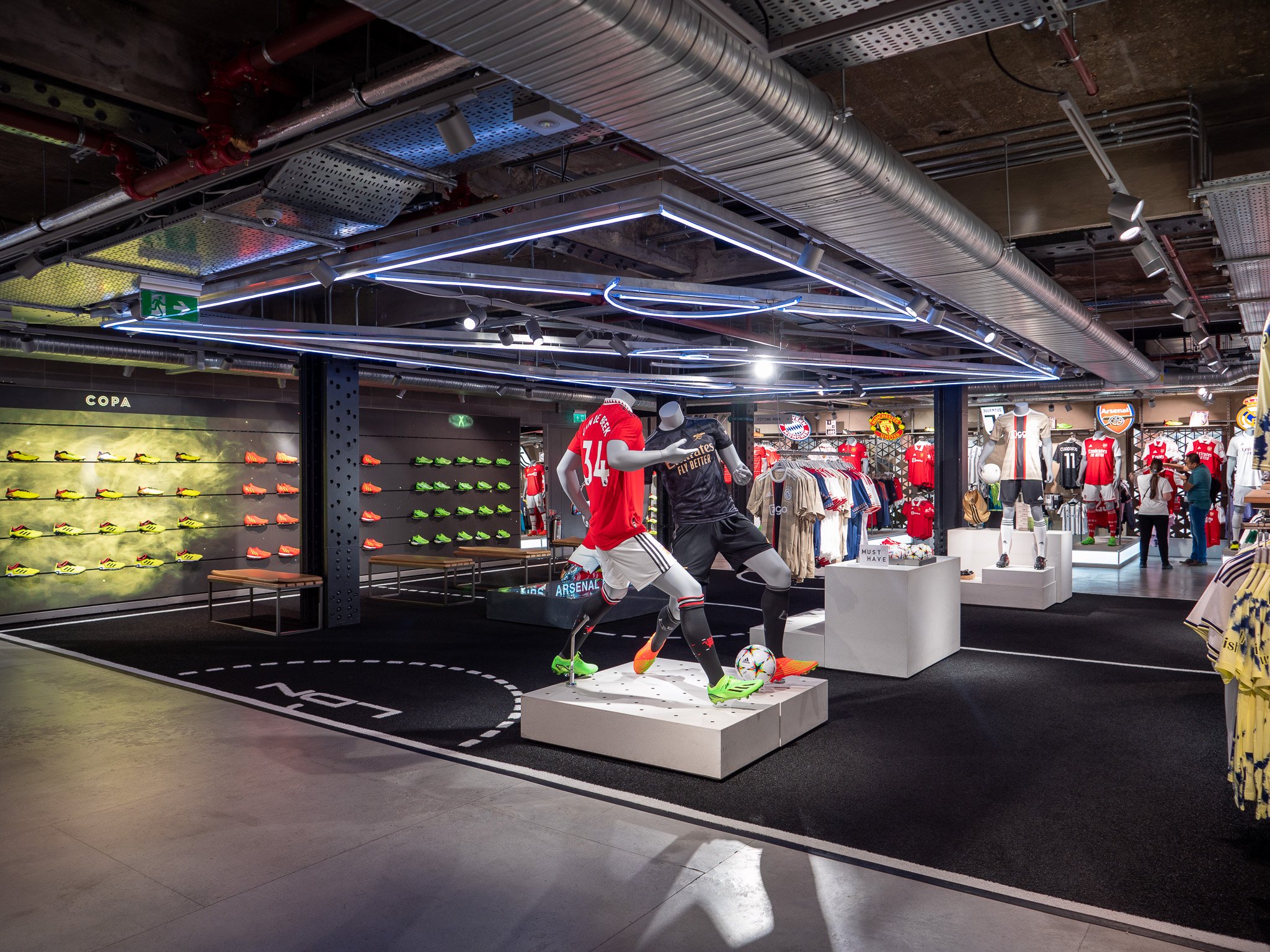 Inside a sports apparel store with soccer merchandise, including mannequins in soccer uniforms, wall-mounted soccer shoes, and shelves with jerseys and shirts.