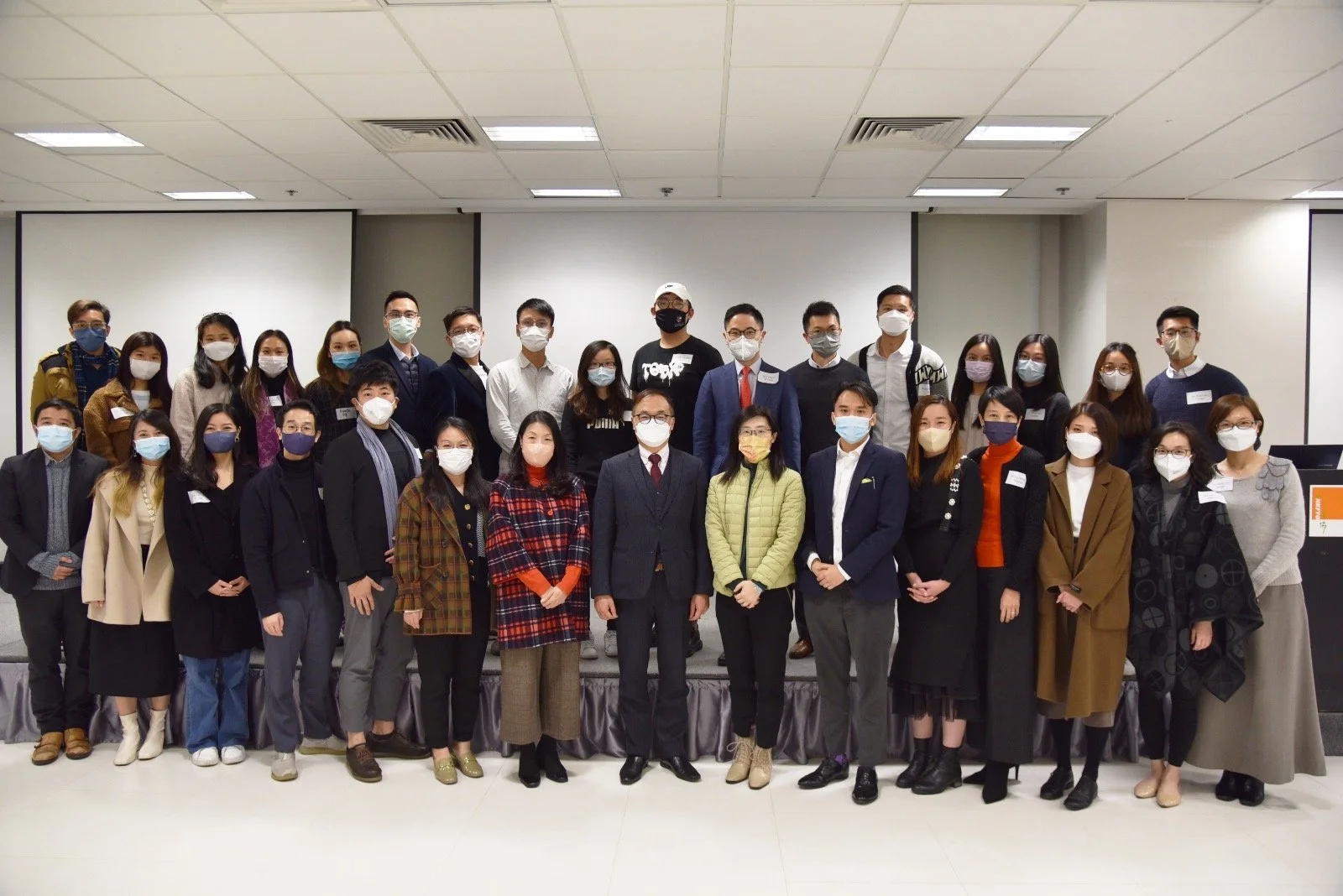 Group of people standing on a stage in a conference room, all wearing masks.