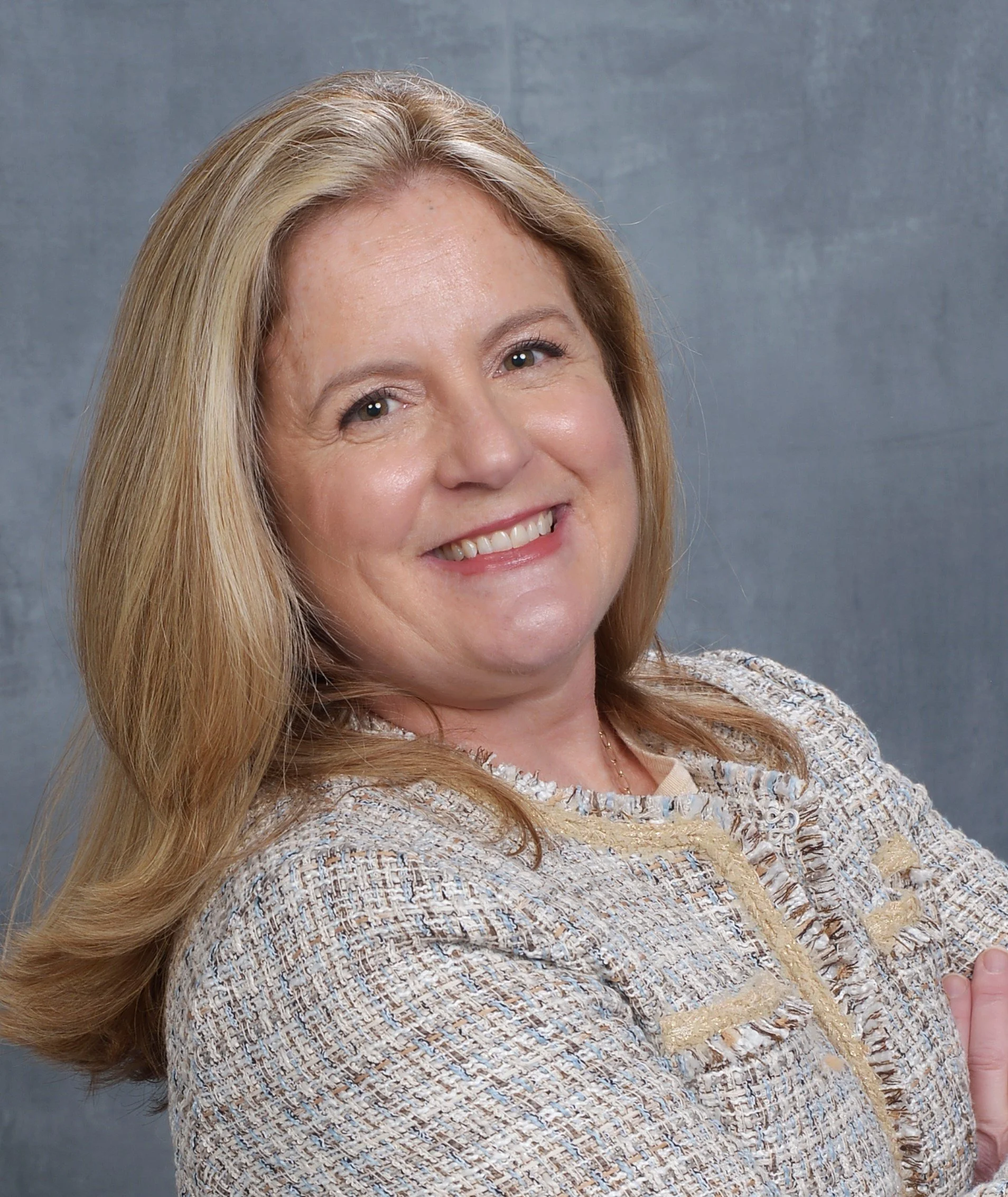 Smiling woman with shoulder-length brown hair outdoors, wearing a blue top with white star patterns, with greenery in the background.