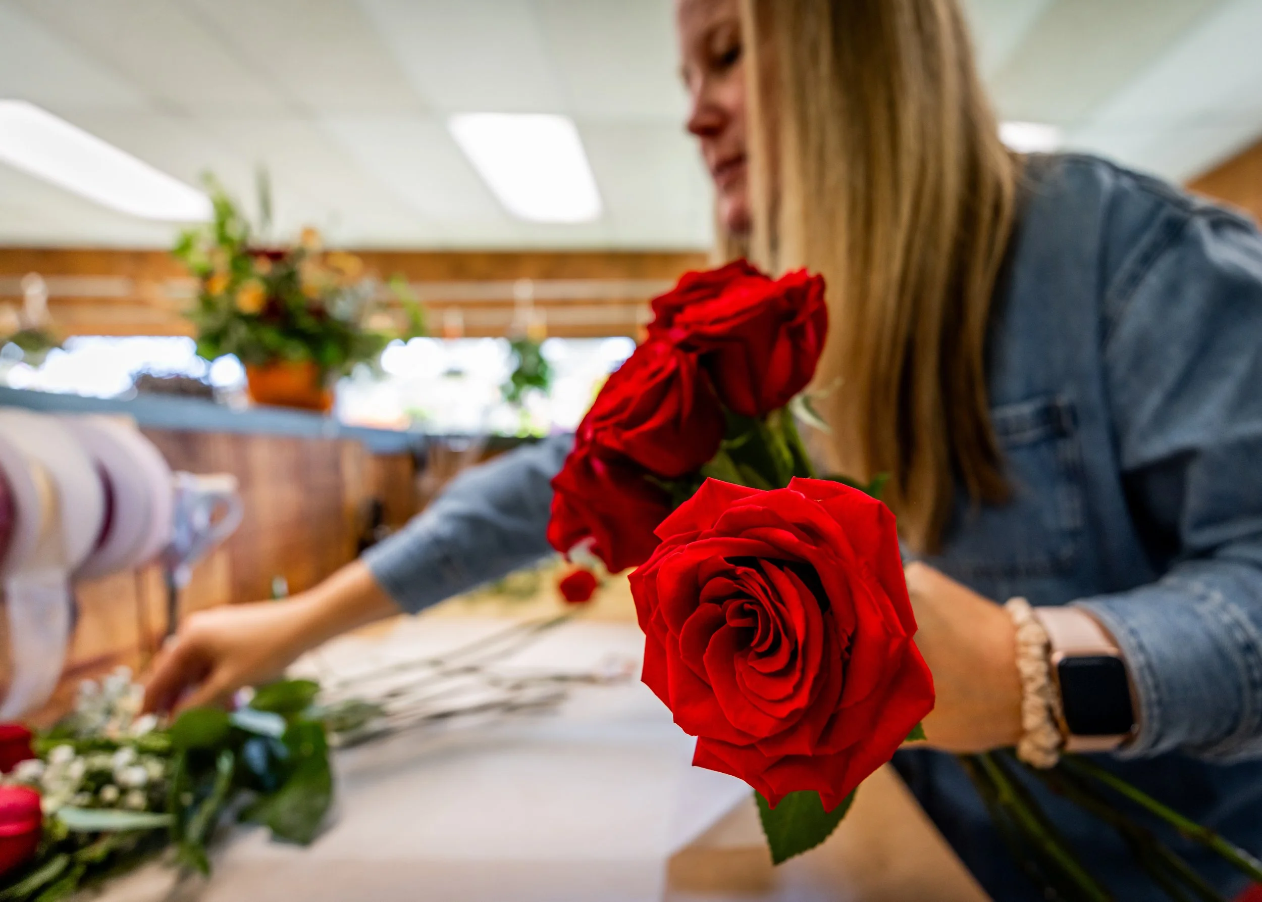 A woman arranges fresh red roses on a table in a floral shop.