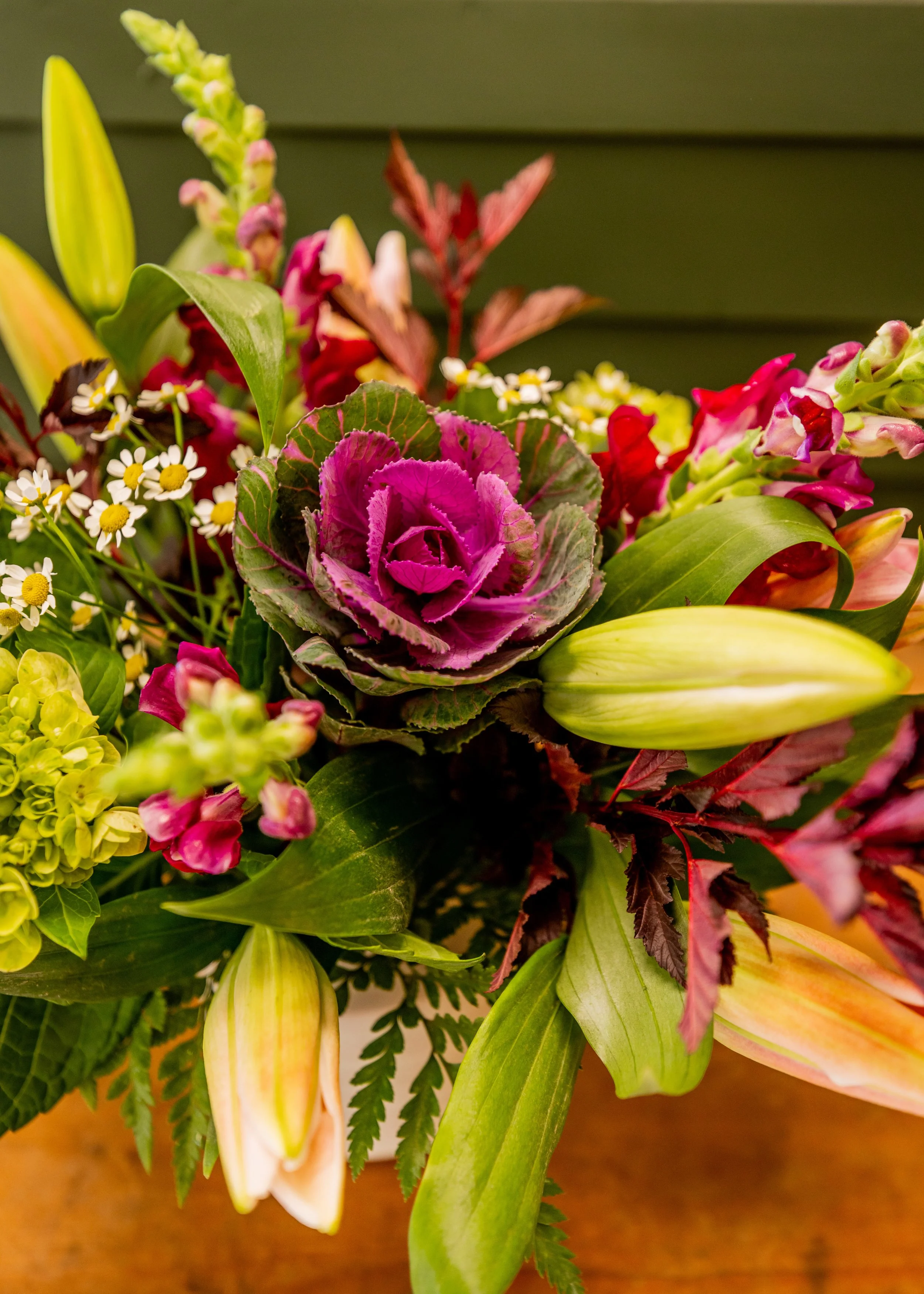 Close-up of a colorful flower bouquet with purple, pink, yellow, and white flowers against a green background.