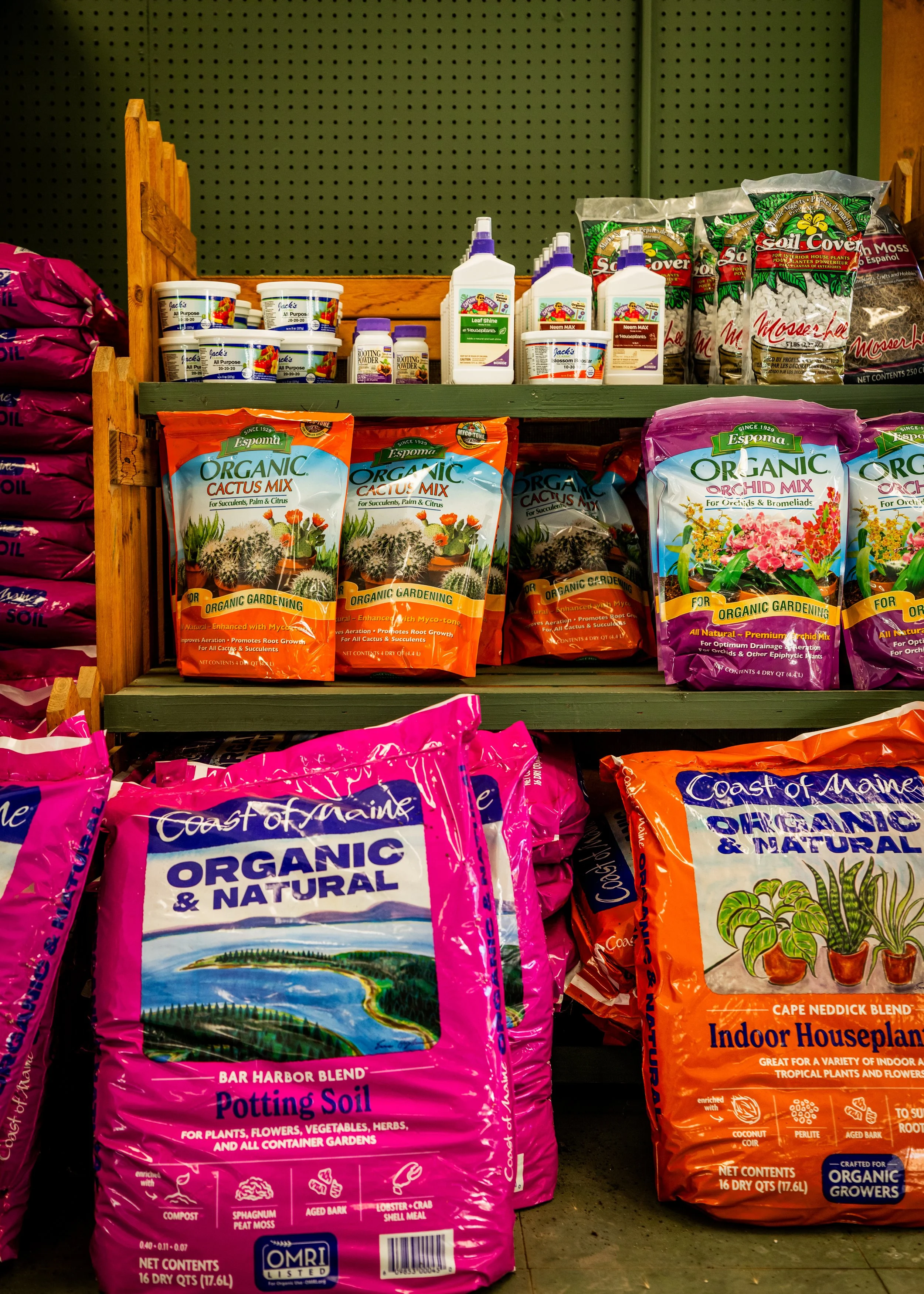 Shelves with gardening supplies, including bags of potting soil, organic cactus mix, orchid mix, and indoor houseplant soil, along with bottles of plant fertilizer and plant care products.