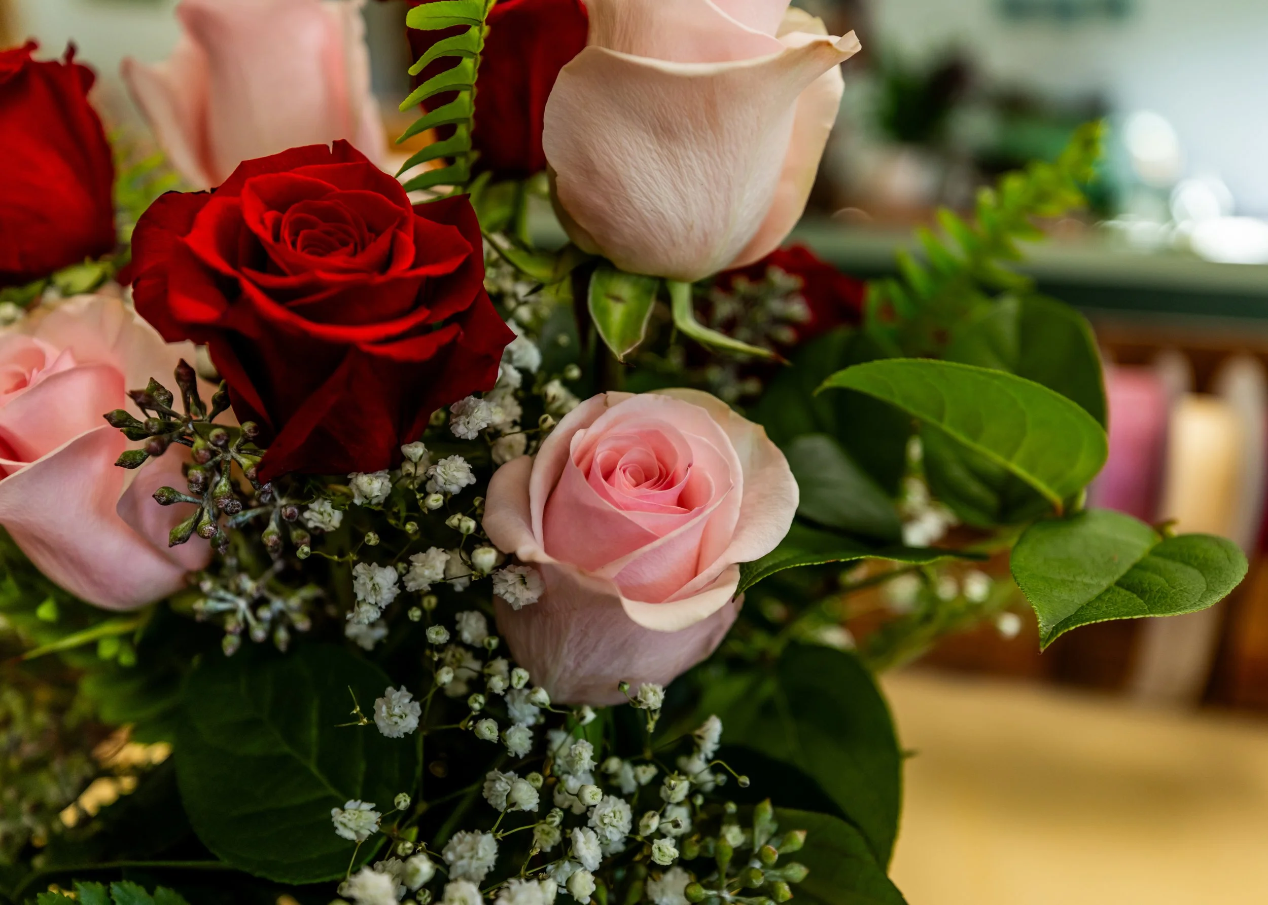 A bouquet of pink, red, and cream roses with white baby's breath flowers and green leaves.