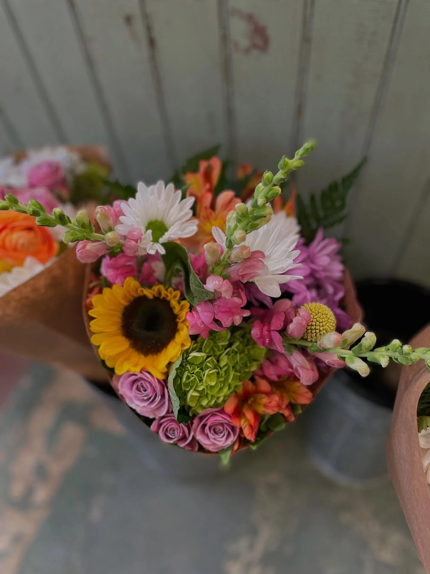 Colorful bouquet of assorted flowers including sunflowers, pink roses, white daisies, and snapdragons.