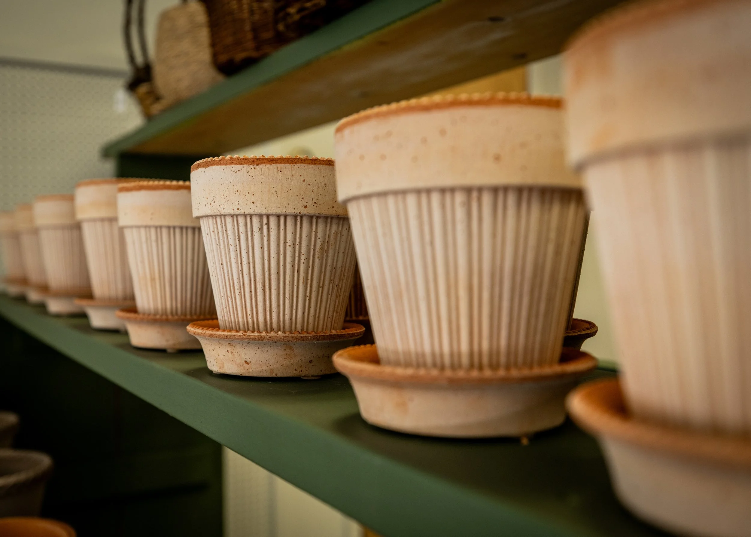 Stacked unglazed ceramic plant pots with ridges on a green shelf.