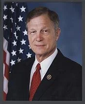 Portrait of a man wearing a suit and tie standing in front of an American flag