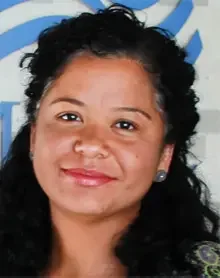 Close-up of a woman with curly black hair and a warm smile, wearing earrings, against a blue background.