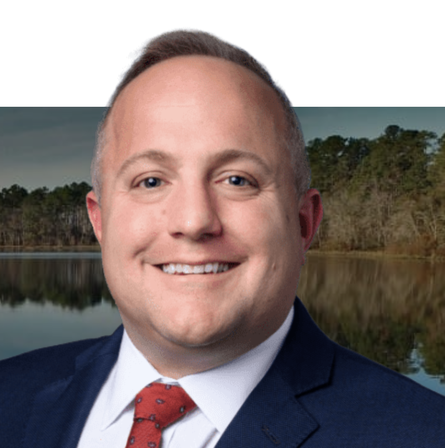 Portrait of a smiling man in a suit and tie with a natural landscape background of a lake and trees.