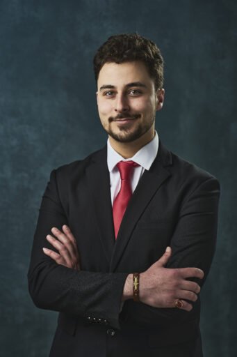 Professional man in a suit and red tie with crossed arms, smiling confidently.