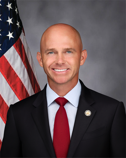 Portrait of a man in a suit and tie, standing next to an American flag.