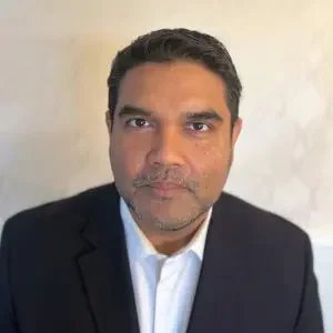 Portrait of a man in a suit and white shirt against a neutral background.