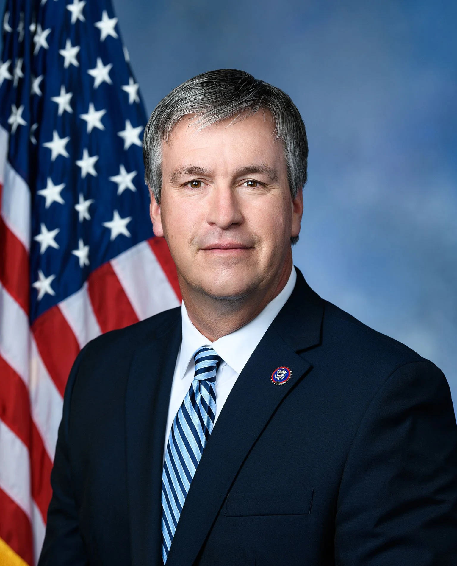 A man in a suit with an American flag in the background.
