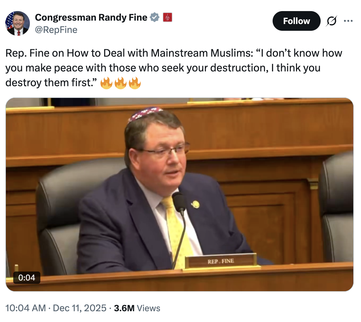 Commissioner Randy Fine speaking at a hearing, seated at a table with a microphone, wearing a dark suit and yellow tie, with a nameplate reading 'REP. FINE', wooden panel background, and an emotional expression.