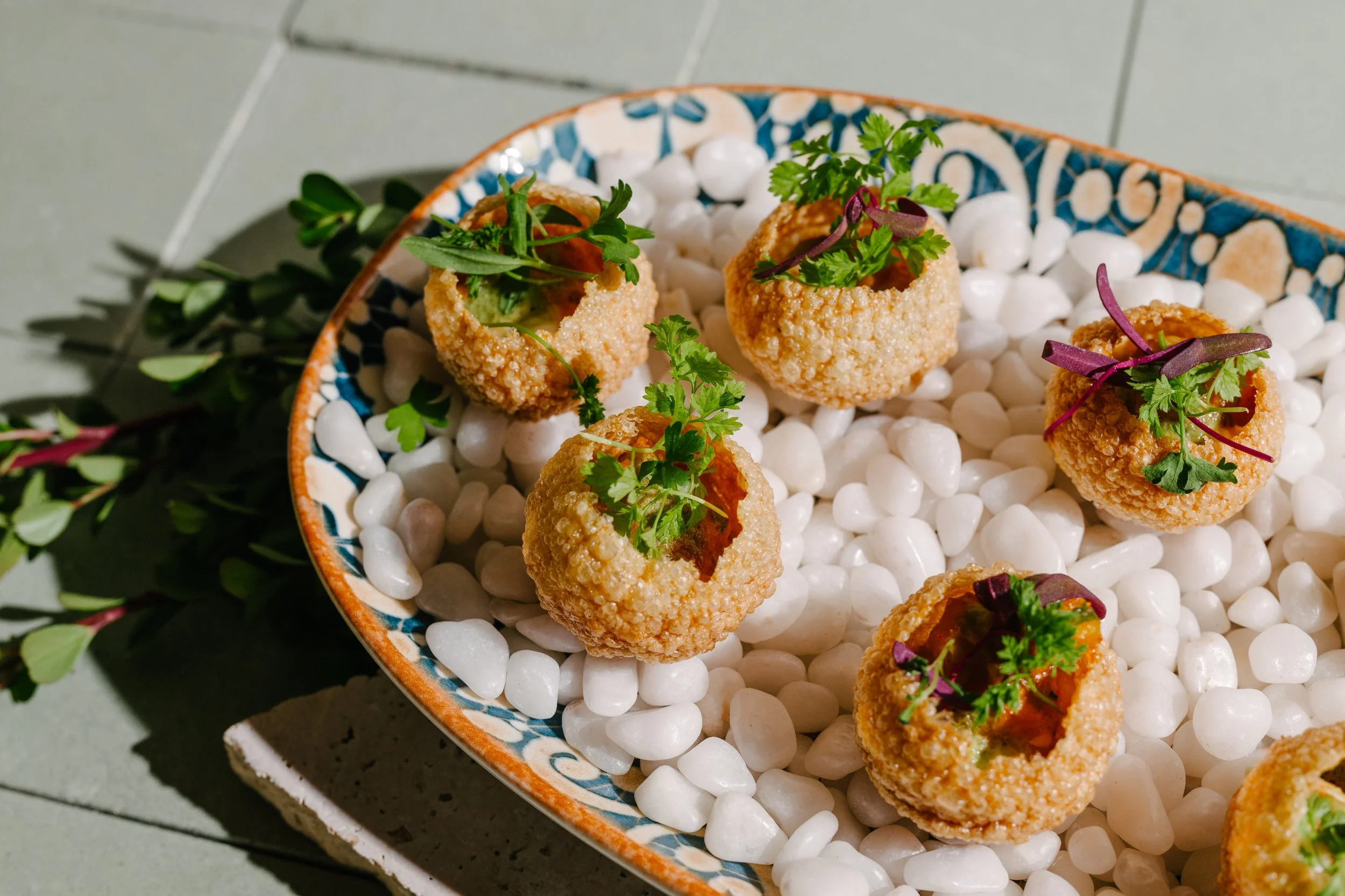 Breaded appetizers topped with herbs, served on white stones in a decorative bowl.