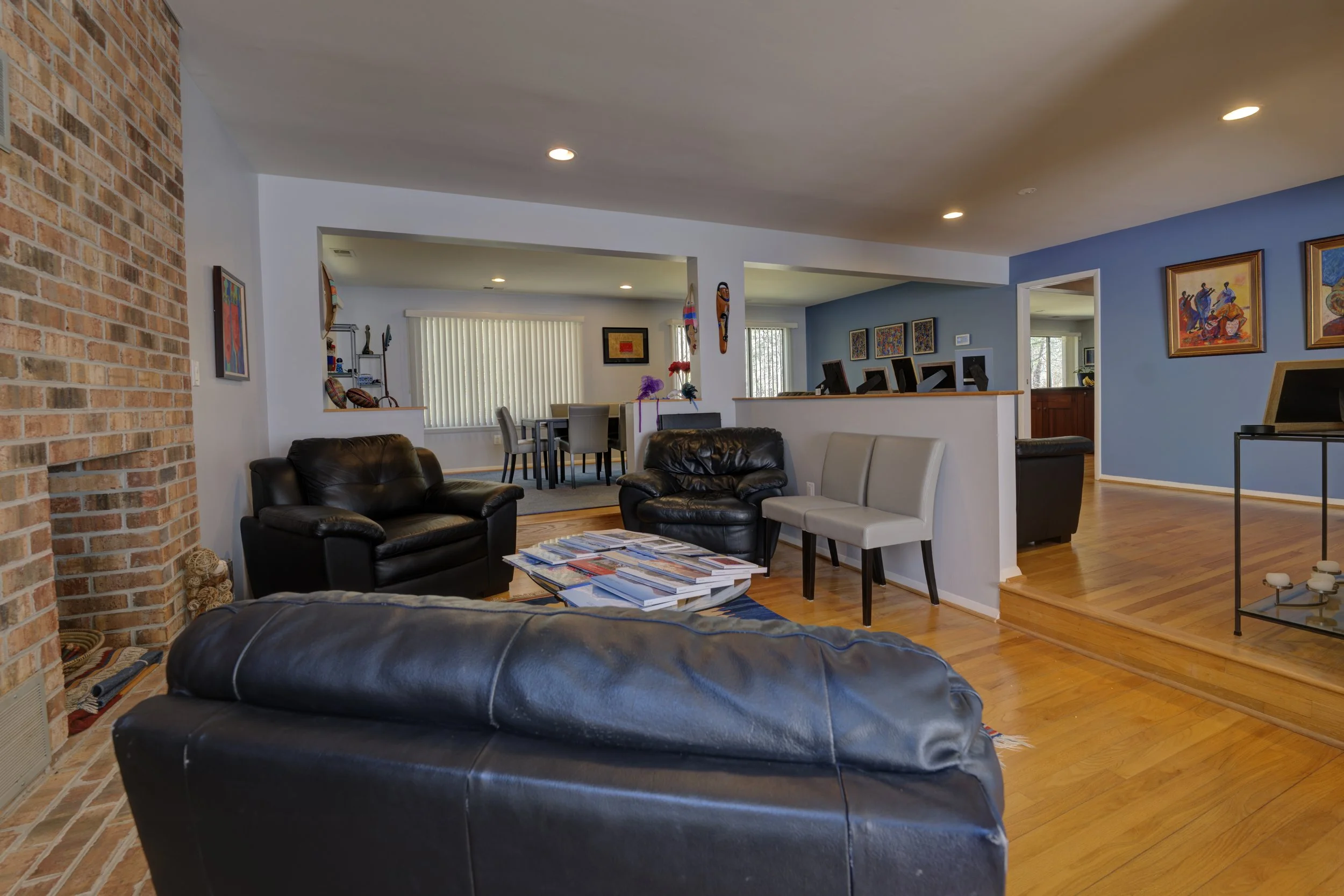 Living room with black leather sofas, a coffee table with magazines, a brick fireplace, and artwork on the walls.