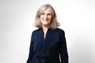 A woman with long blonde hair wearing a navy blue blouse with a bow tie, smiling at the camera.