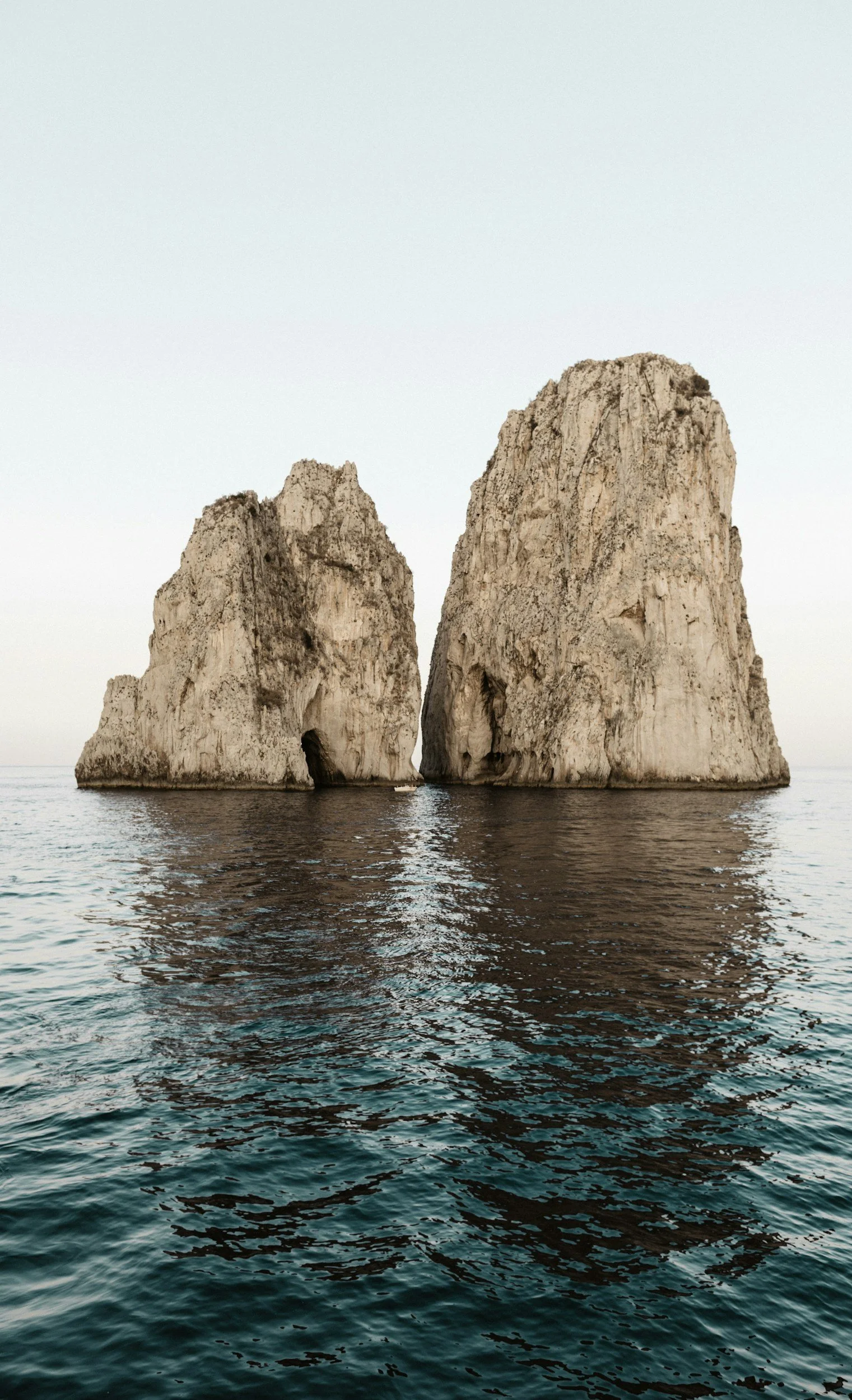 Two large sea stacks rising from the water, with a narrow gap between them, under a pale sky.