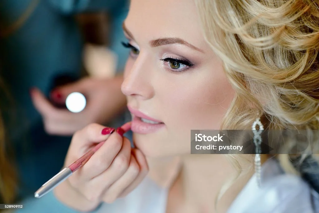 Frau erhält im Schönheitsstudio Make-up, die Kosmetikerin trägt einen Lippenstift auf die Lippen der Frau auf.