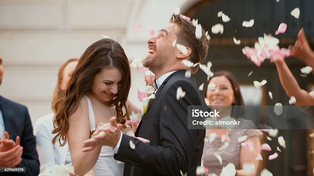 Braut und Bräutigam feiern auf einer Hochzeit, umgeben von Freunden, während Konfetti fällt.