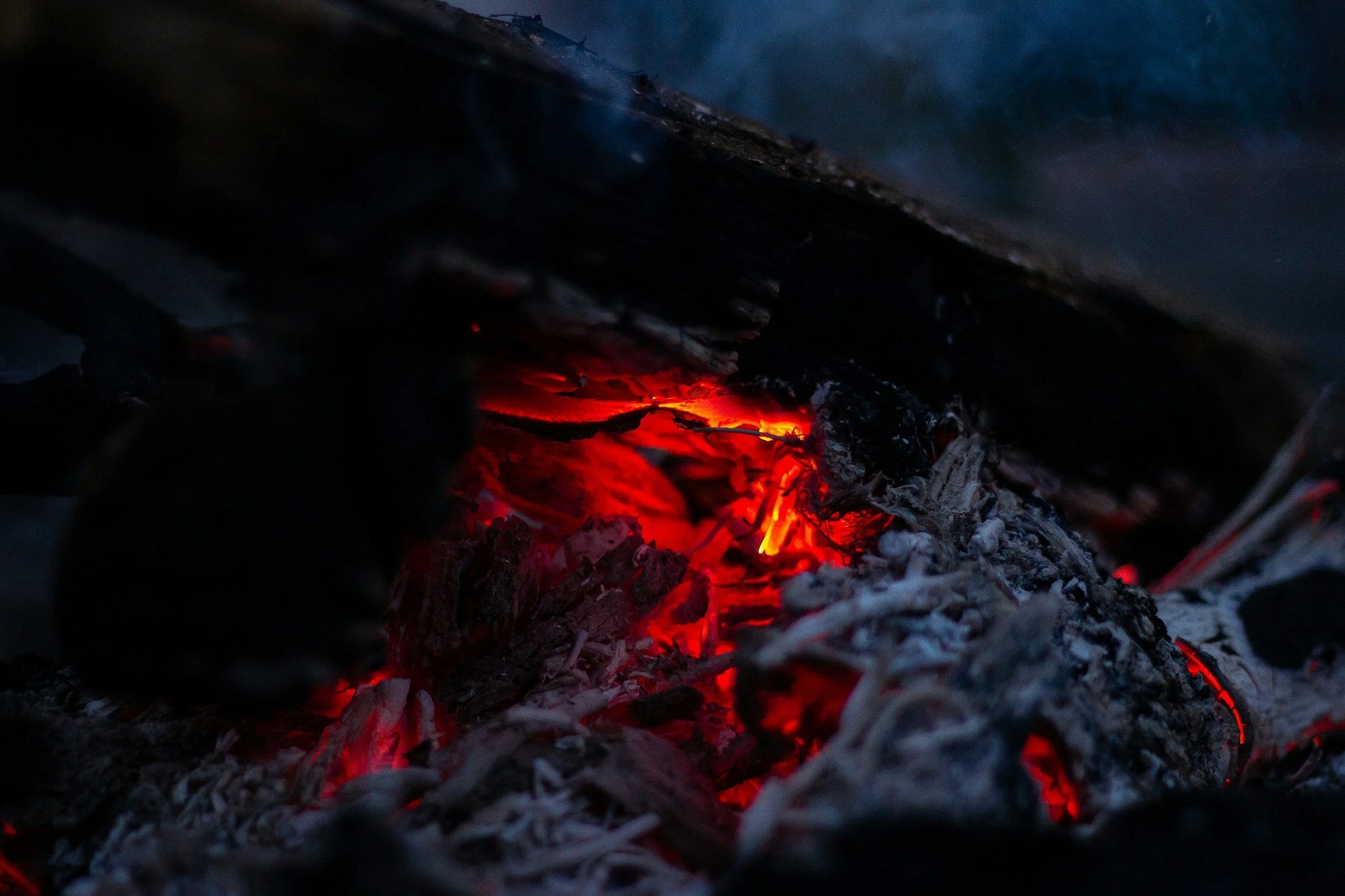 Close-up view of glowing red and orange embers and ashes from a fire.