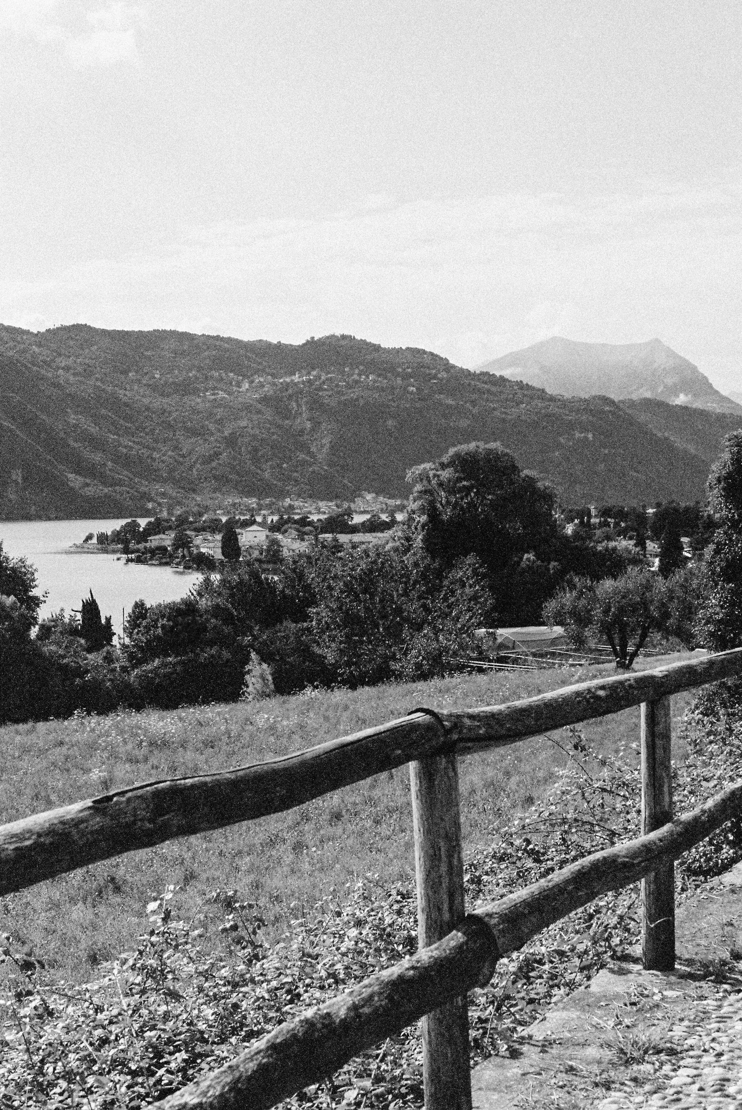 Black and white film photograph of Lake Como, Italy overlooking alpine mountains and valley with rustic wooden fence — Italy travel photographer Anna Hudson