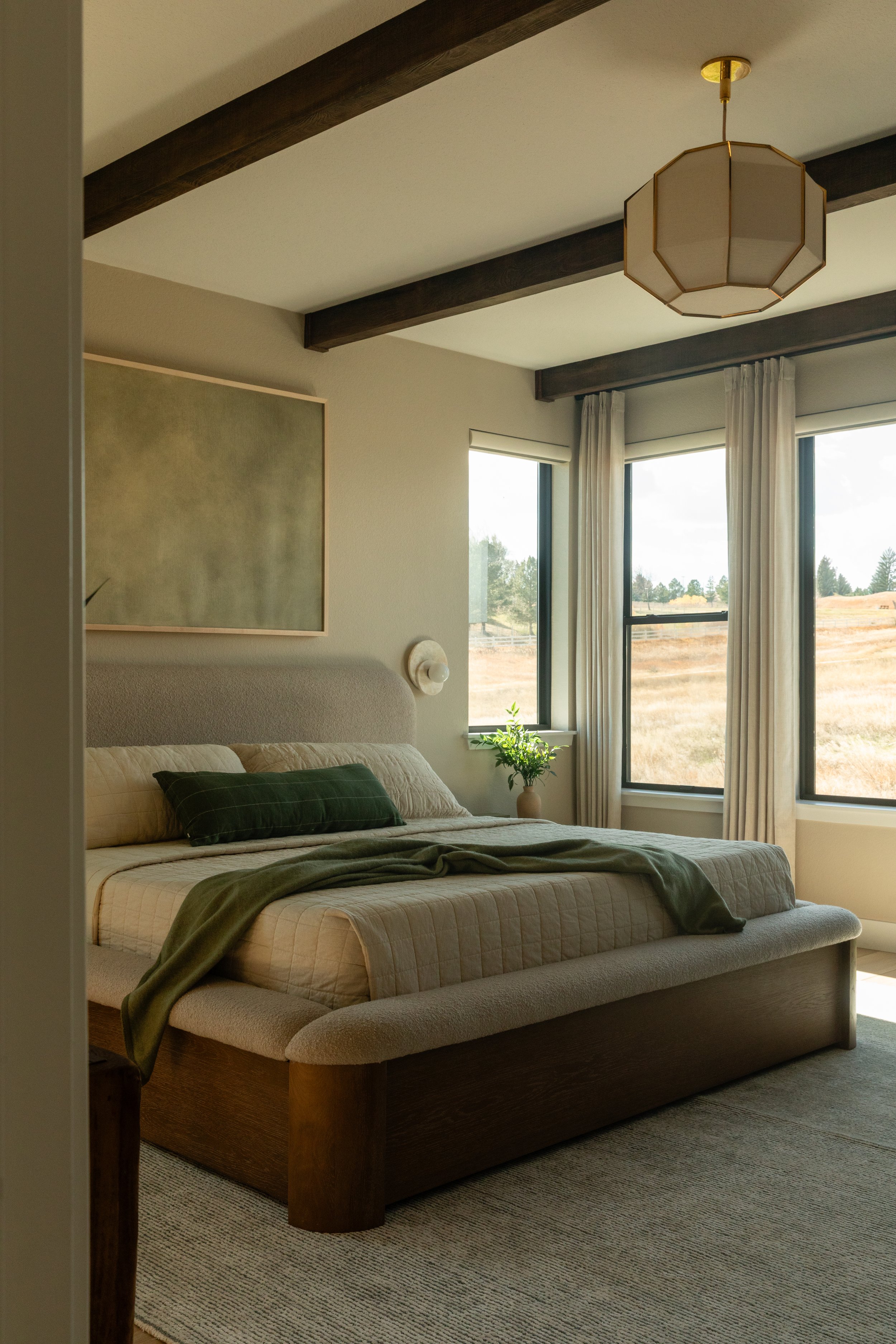 Modern master bedroom with exposed beams, sage green accents, and Colorado landscape views — Denver interior design photographer Anna Hudson