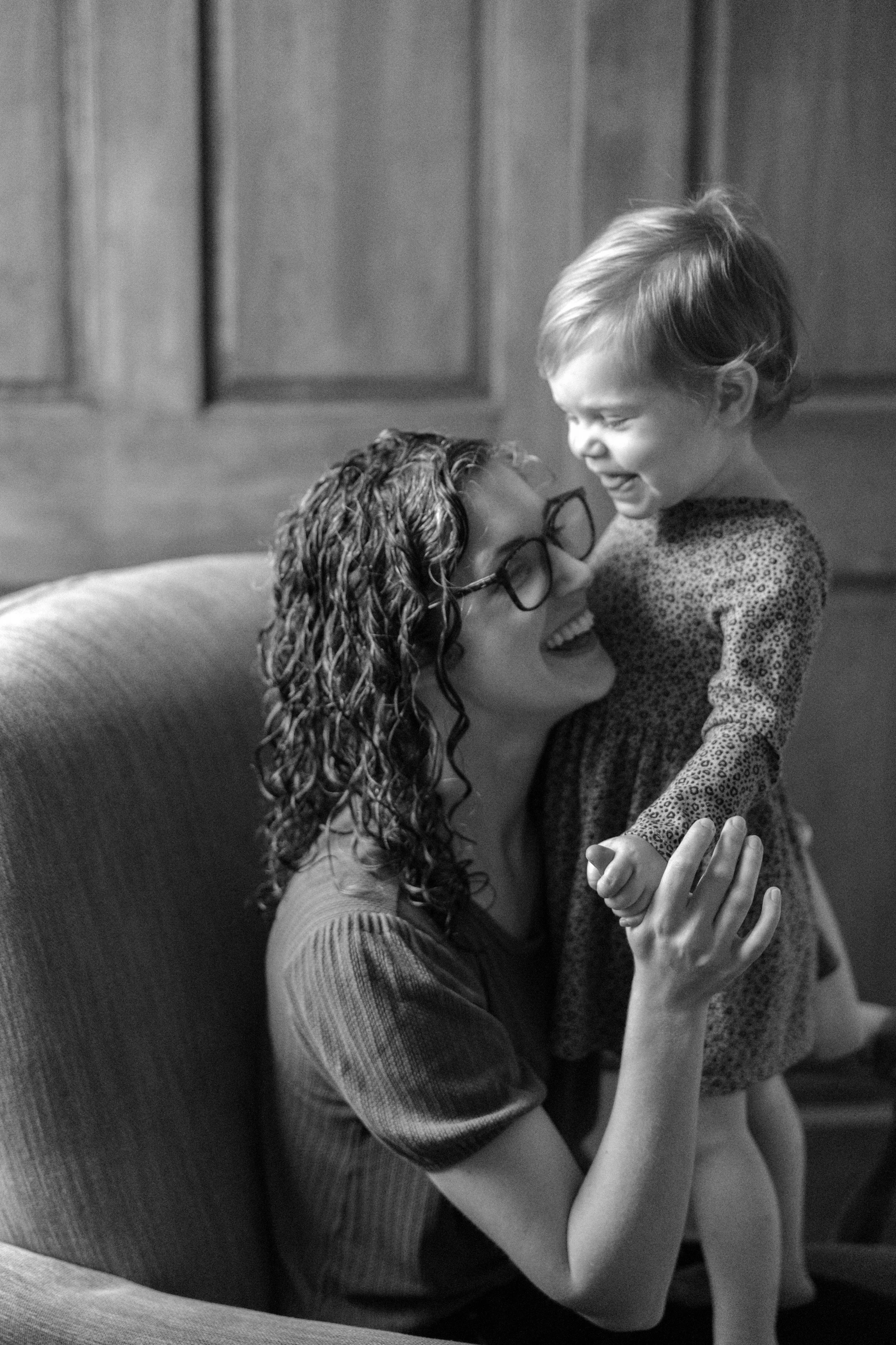 Black and white candid portrait of a mother laughing and lifting her young daughter in a rocking chair — family photographer Anna Hudson
