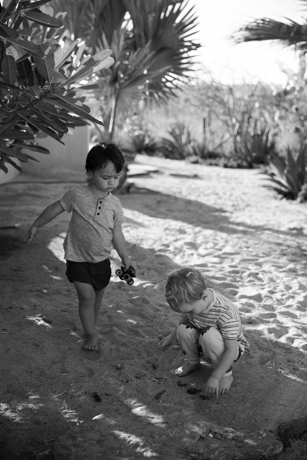 Black and white candid portrait of two young children playing in the sand in Todos Santos, Baja, Mexico — family photographer Anna Hudson