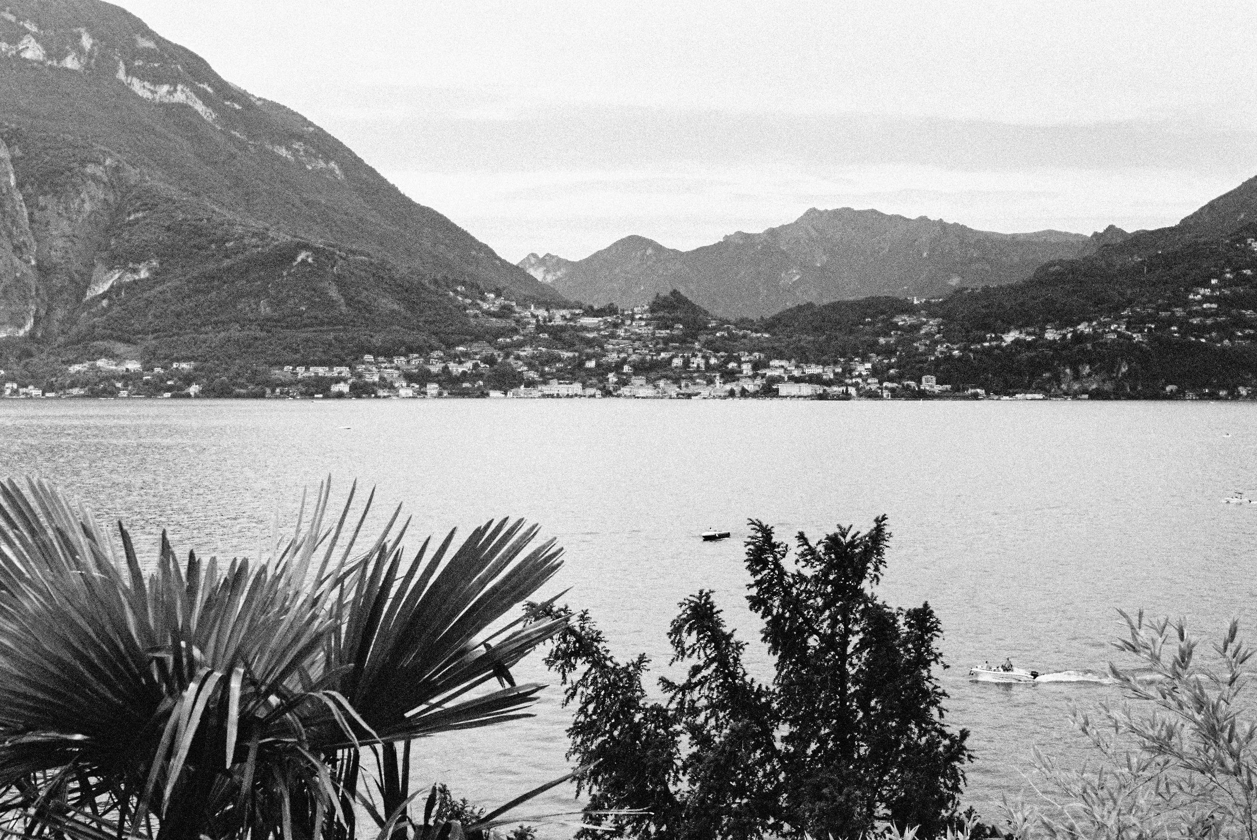 Black and white film photograph of Lake Como panorama from Varenna, with Menaggio and the Alps visible across the water — Italy travel photographer Anna Hudson