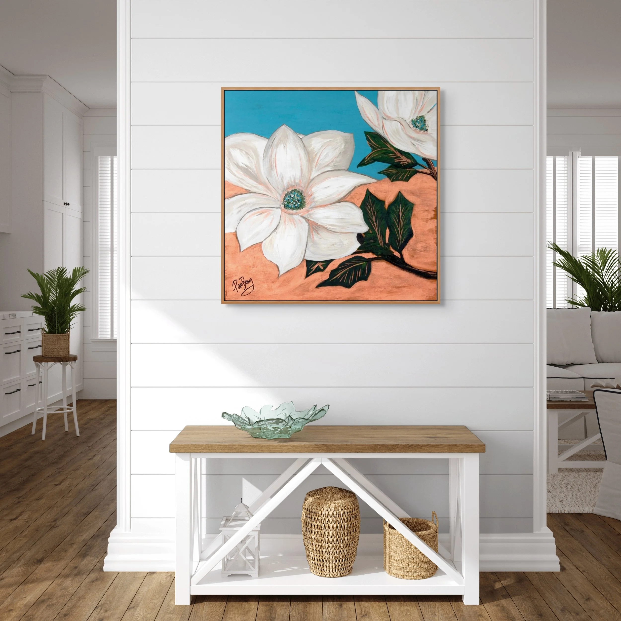 A colorful painting of white flowers with green leaves and a blue background hanging on a white shiplap wall in a bright living room with hardwood floors, a white console table with a glass bowl on top, and woven baskets underneath.