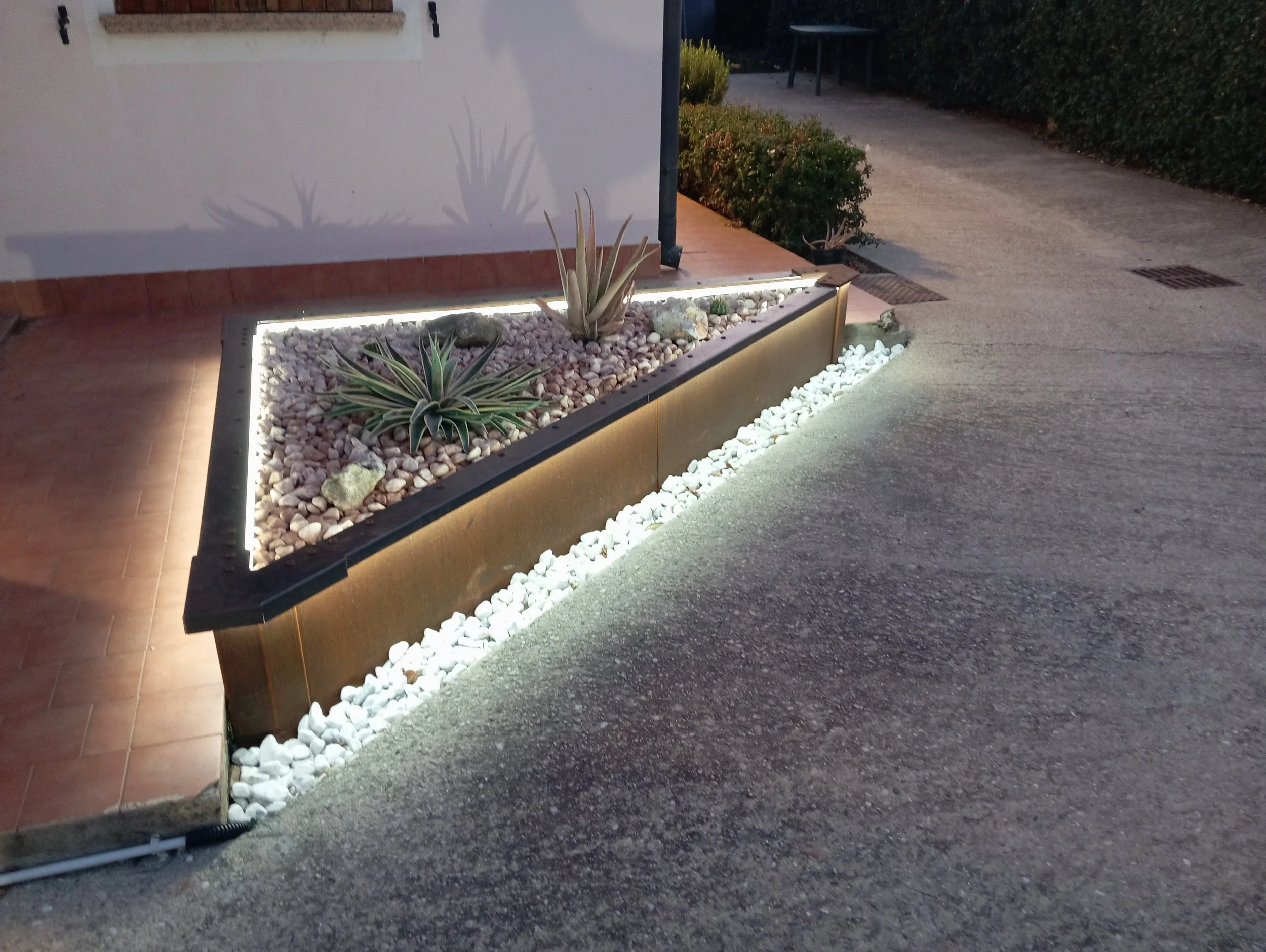 Sistema di bordure rialzate Vault in Corten che delimita un giardino di piante grasse e ghiaia rosa, illuminato dalla luce solare.