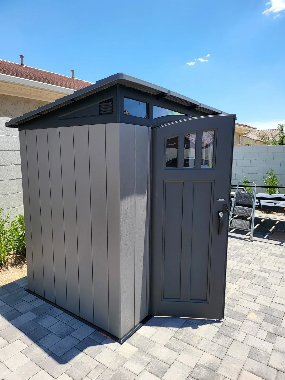Gray resin storage shed with a windowed door assembled on a paver patio in the Phoenix, AZ area by Helping Hands Household Solutions