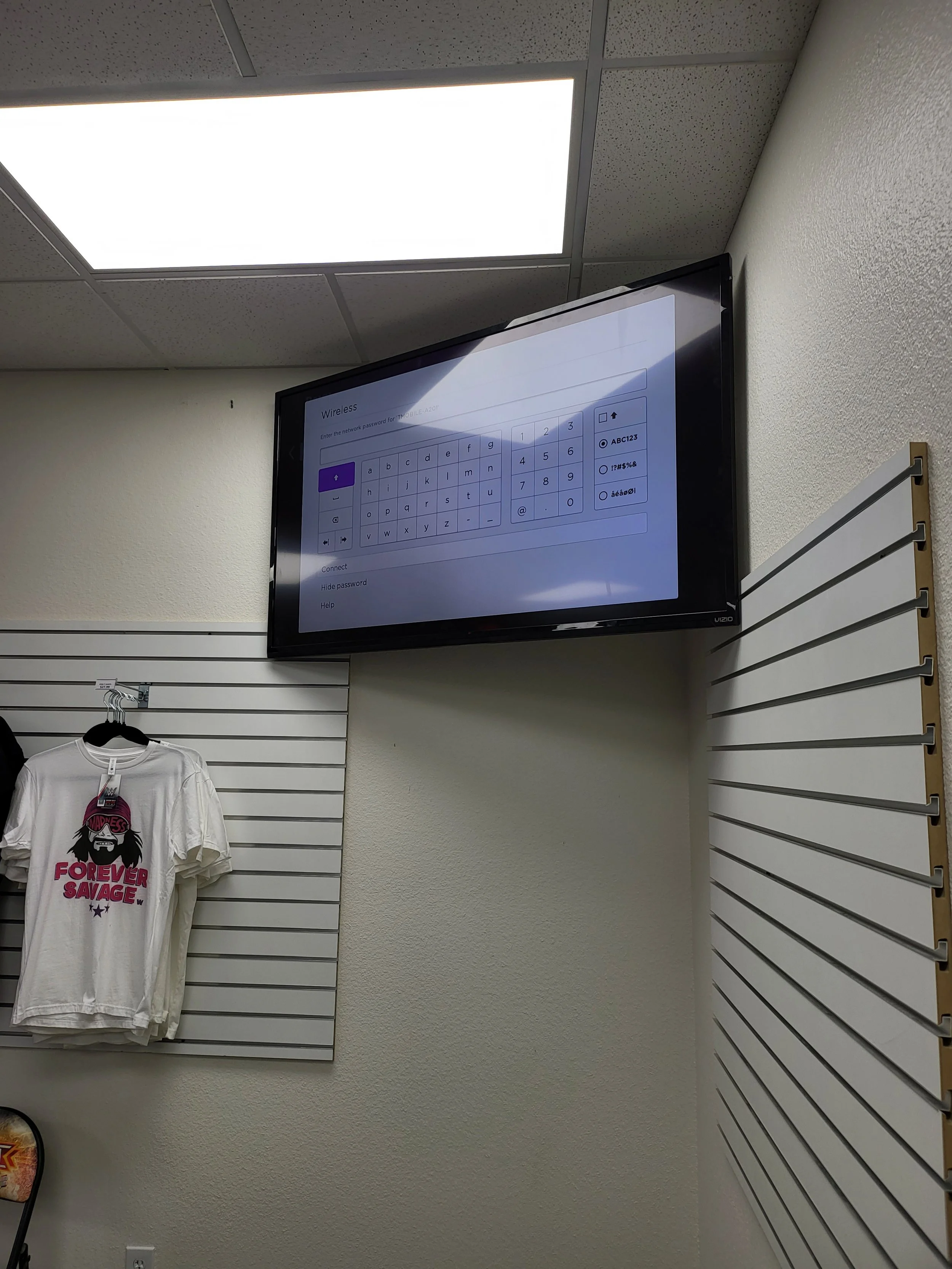 Commercial digital display wall mounting inside a Phoenix retail shop, featuring drop-ceiling wire concealment, commercial-grade wall brackets, and seamless integration above merchandise displays.