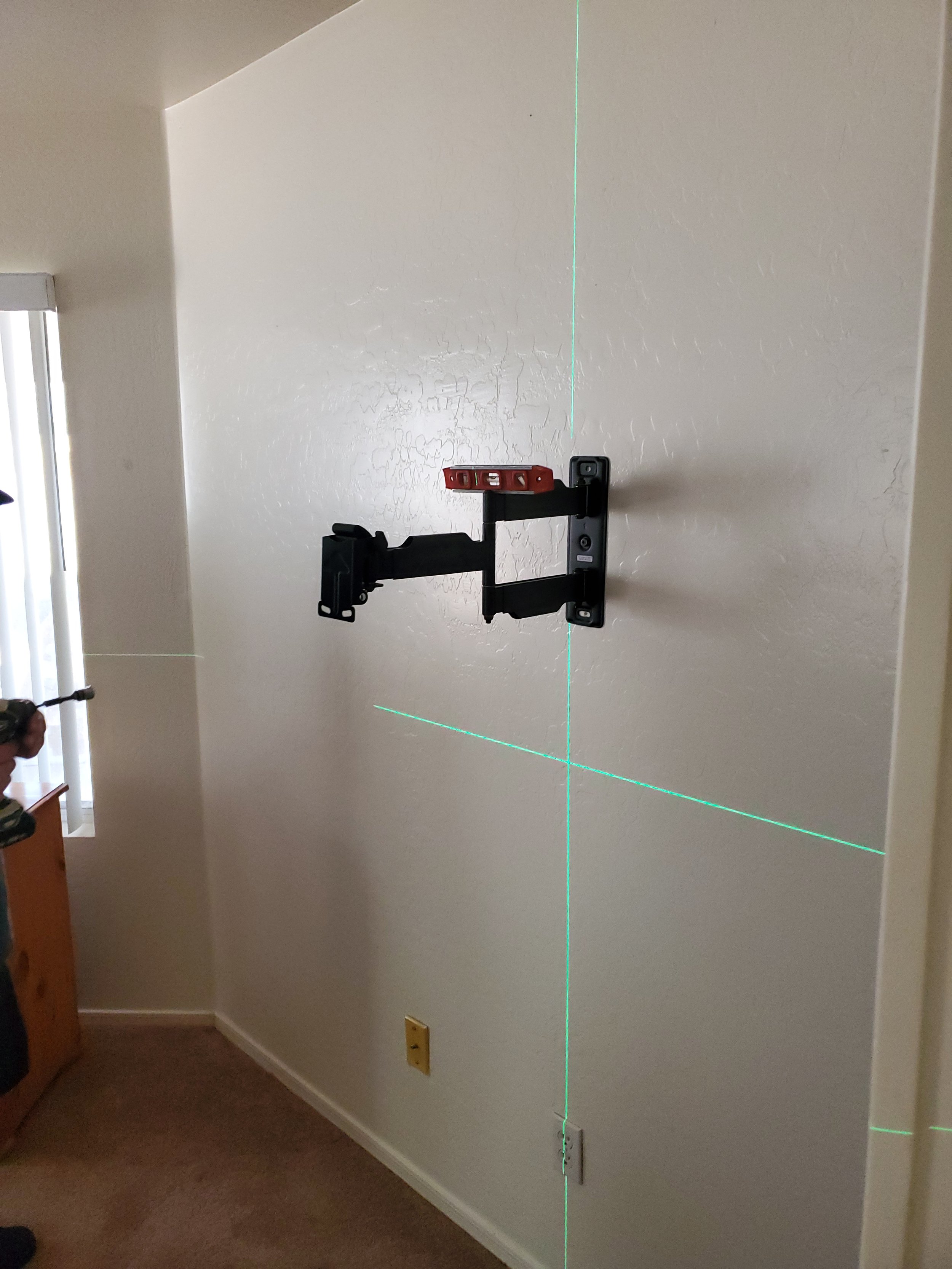 Precision laser-guided TV wall mounting in Phoenix, AZ, utilizing crosshair laser leveling tools for perfectly plumb bracket alignment and accurate stud anchoring on drywall.
