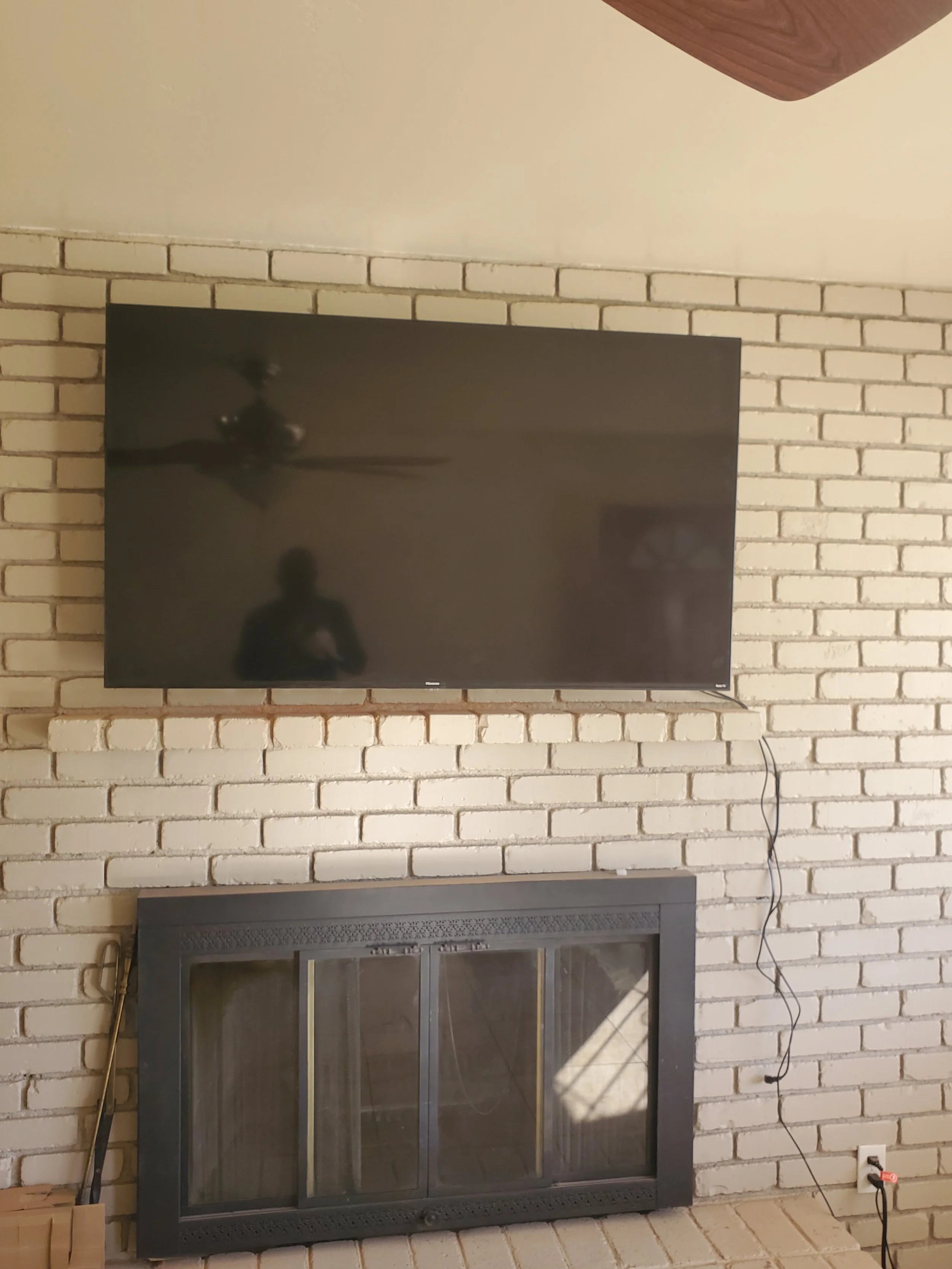 Television mounted over a white brick fireplace hearth, featuring specialized masonry fasteners and clean wire management integrated into an updated living room wall.