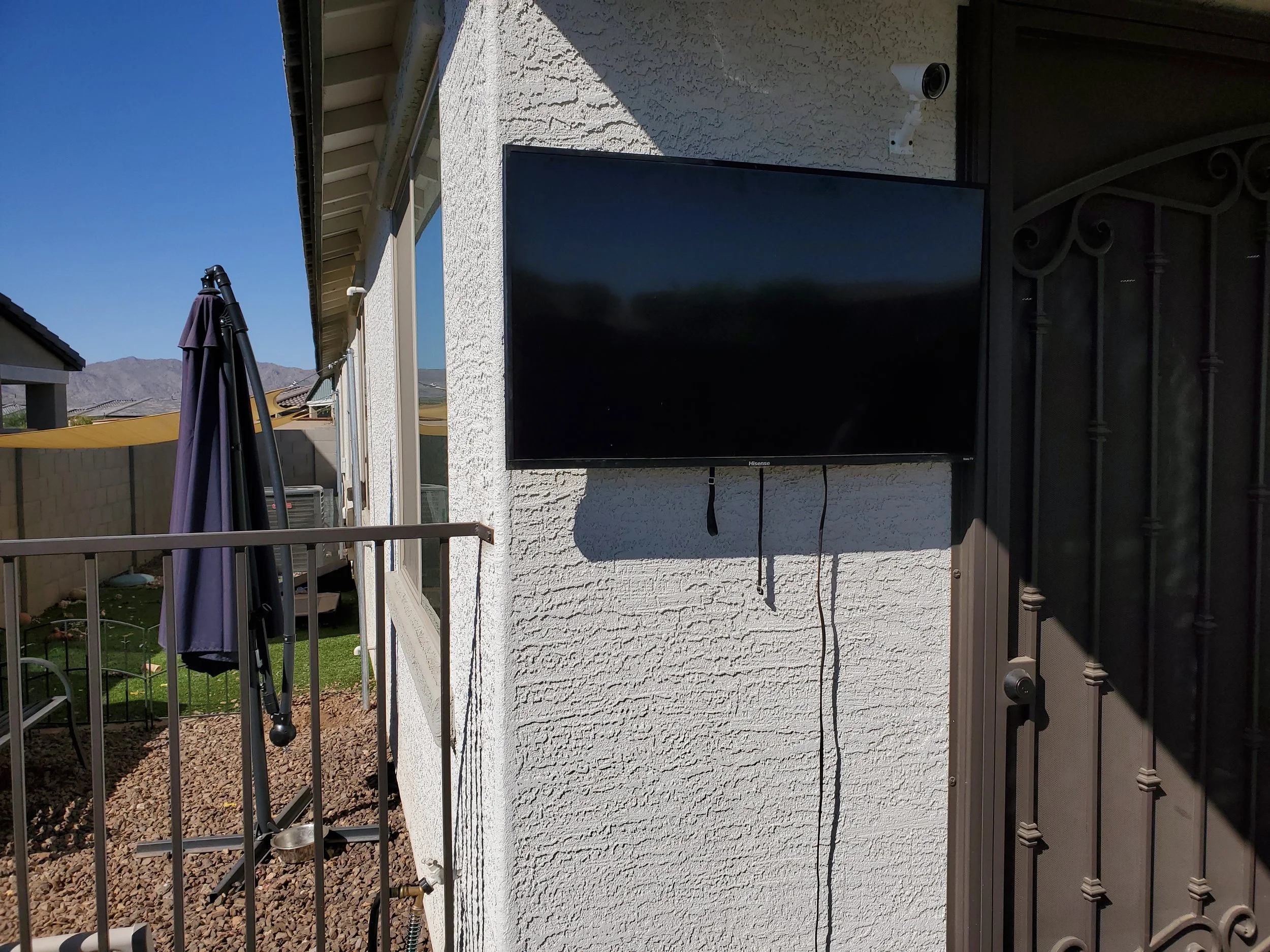 Outdoor patio TV installation on exterior white stucco in Phoenix, AZ, featuring heavy-duty weatherproof wall anchors and secure exterior mounting next to a backyard covered patio area.