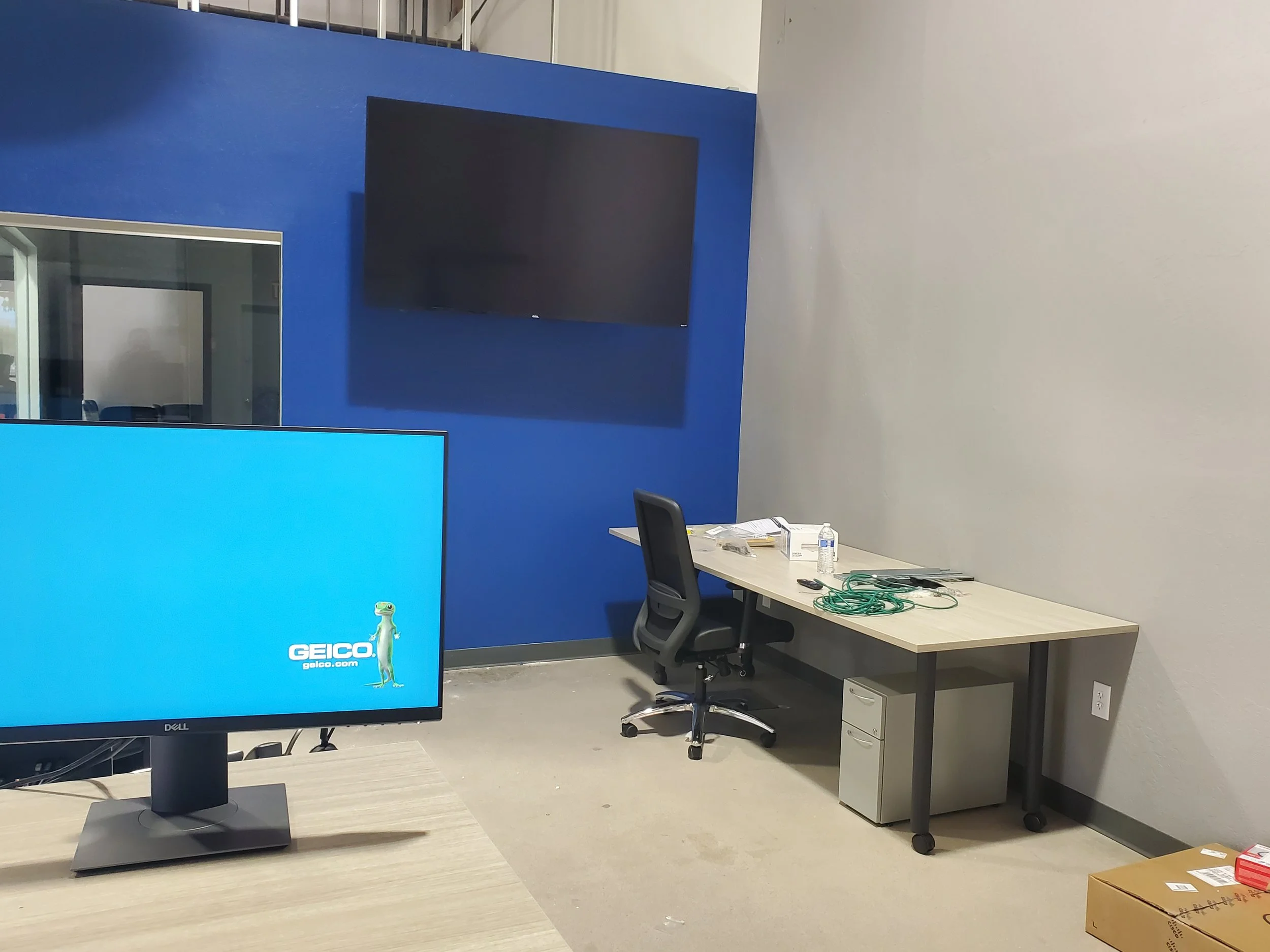 Commercial wall-mounted display installed on a blue accent feature wall inside a corporate office space, featuring hidden cable management and heavy-duty drywall anchors.