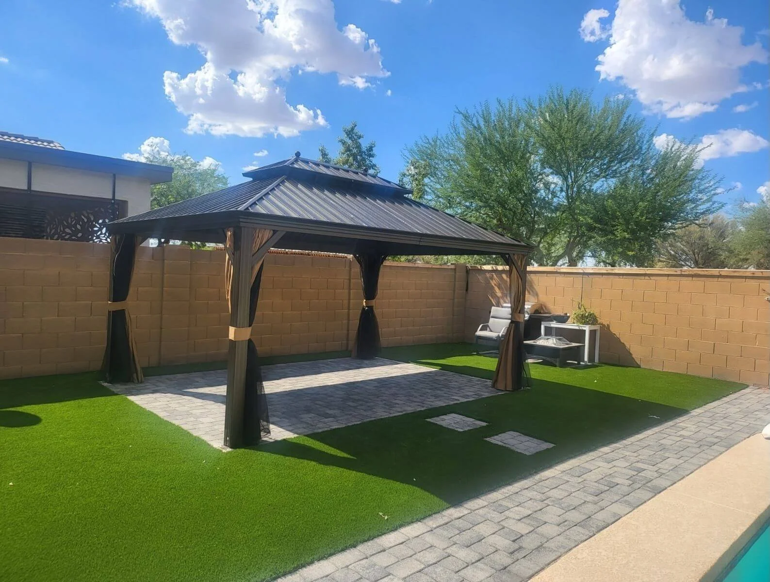 Professional gazebo installation by Helping Hands Household Solutions featuring a tiered hardtop metal gazebo with mesh curtains on a paver patio and artificial grass lawn in Maricopa County.