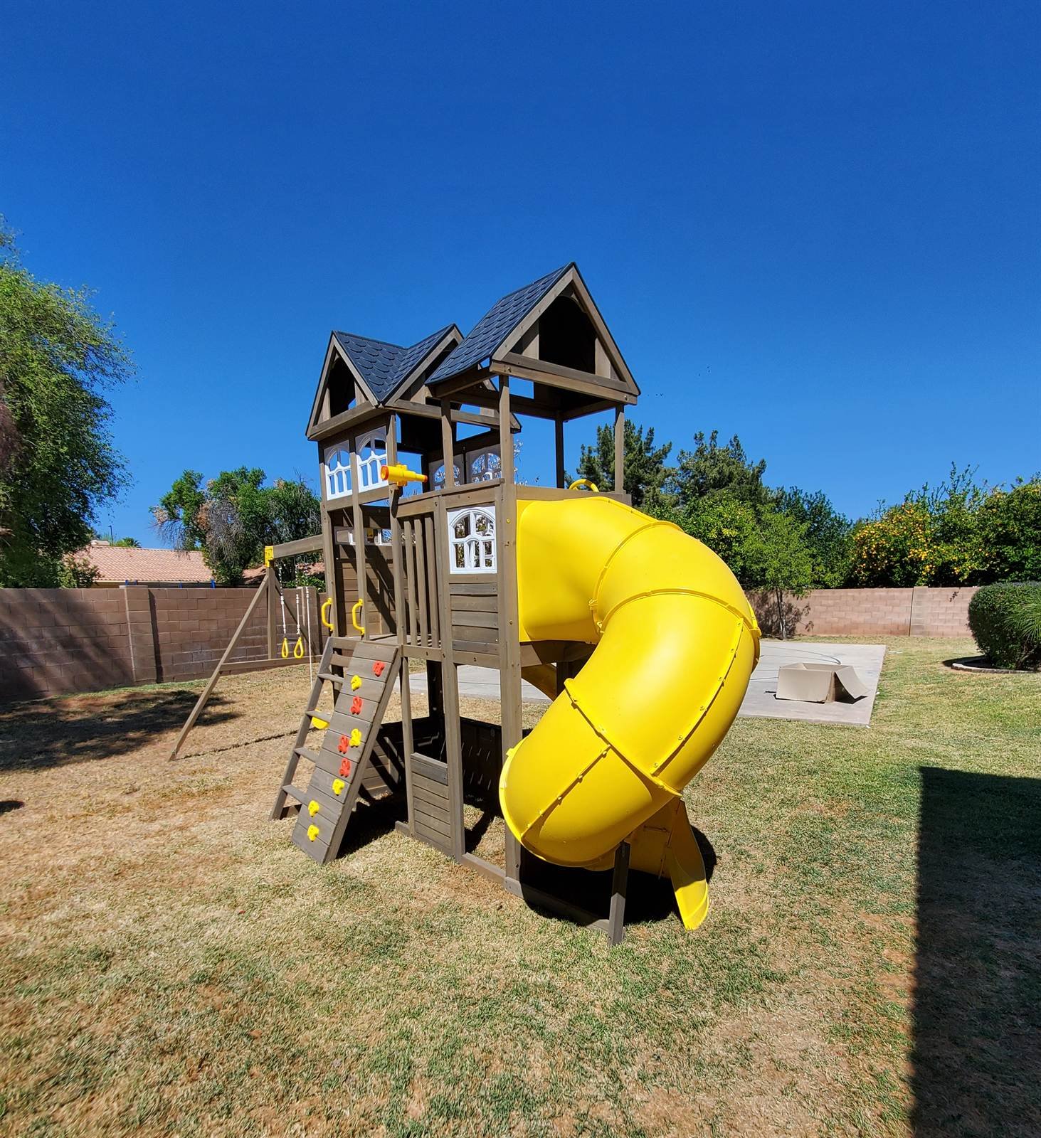 Wooden playset with yellow tube slide and rock wall assembled in a Glendale backyard