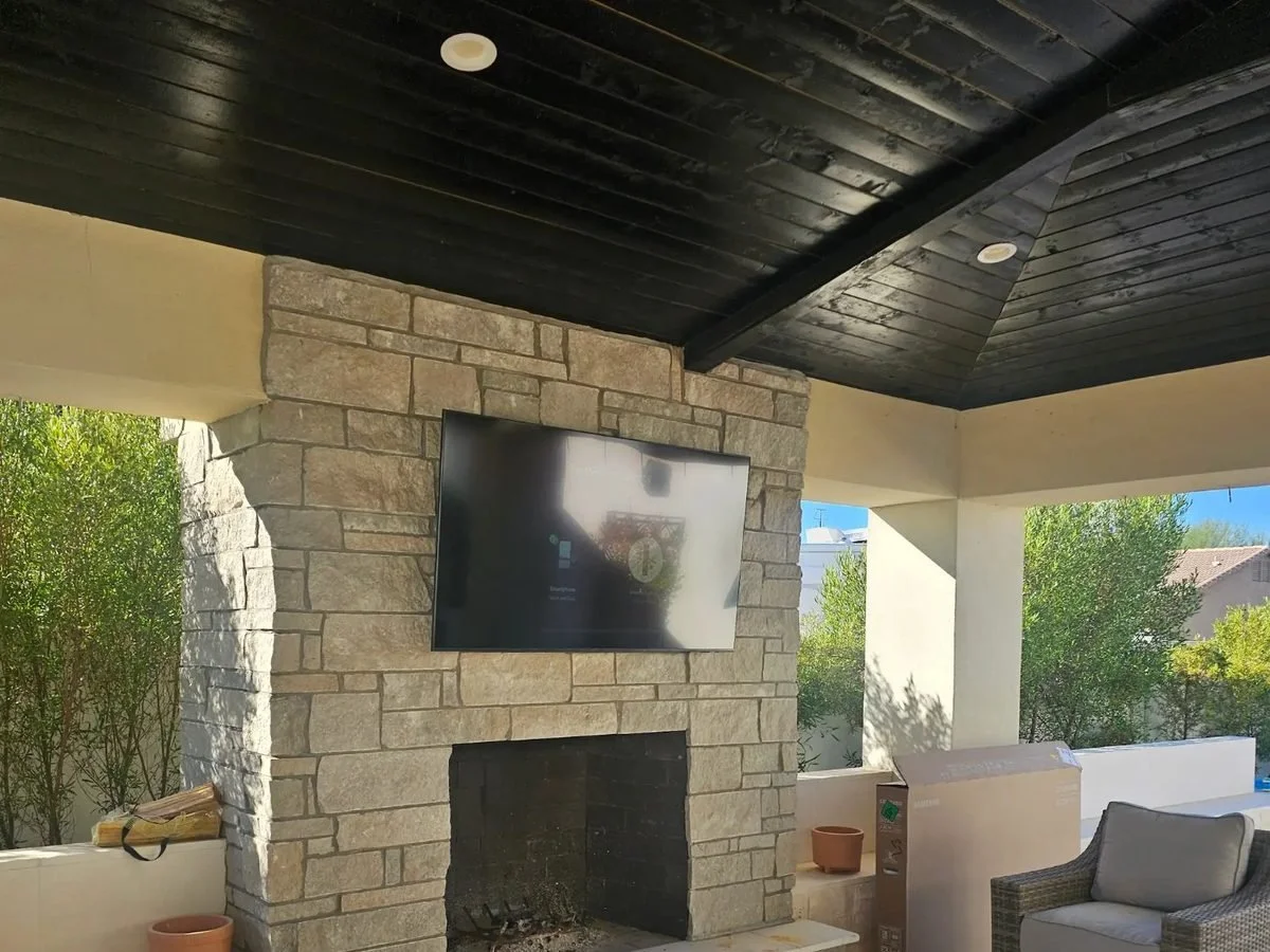 Outdoor TV mounted over a stone patio fireplace in Phoenix by Helping Hands