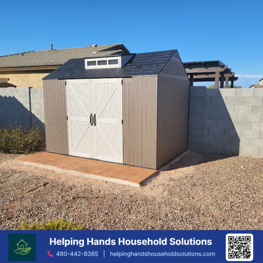 Durable resin outdoor storage shed with barn-style double doors, a gable roof vent, and weatherproof tan panel siding, professionally installed on a paver base in a Phoenix, AZ backyard by Helping Hands Household Solutions — the perfect backyard stor