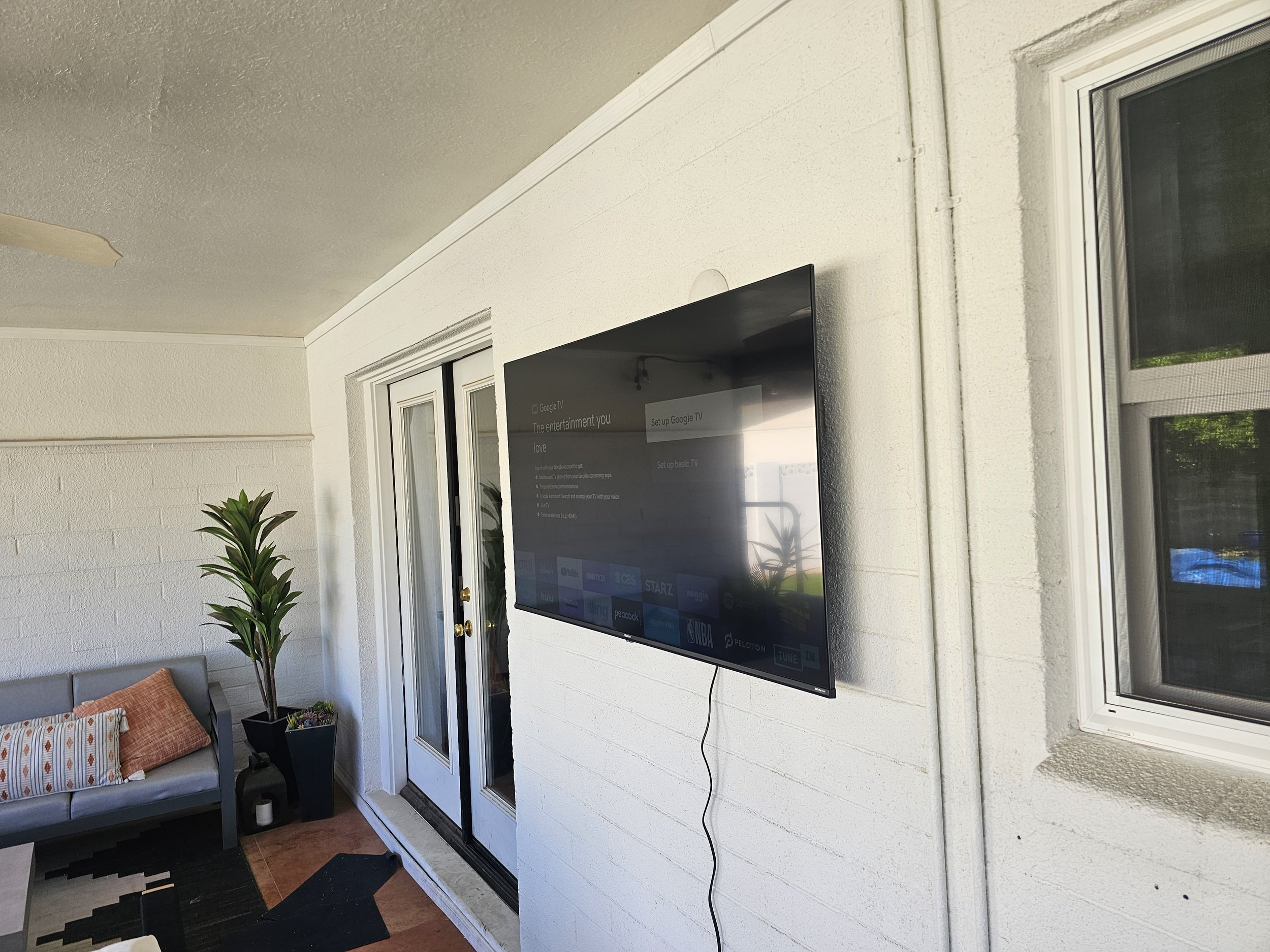 Outdoor patio TV wall mounting on painted exterior brick in Phoenix, AZ, featuring weather-resistant masonry anchoring adjacent to an outdoor seating area.
