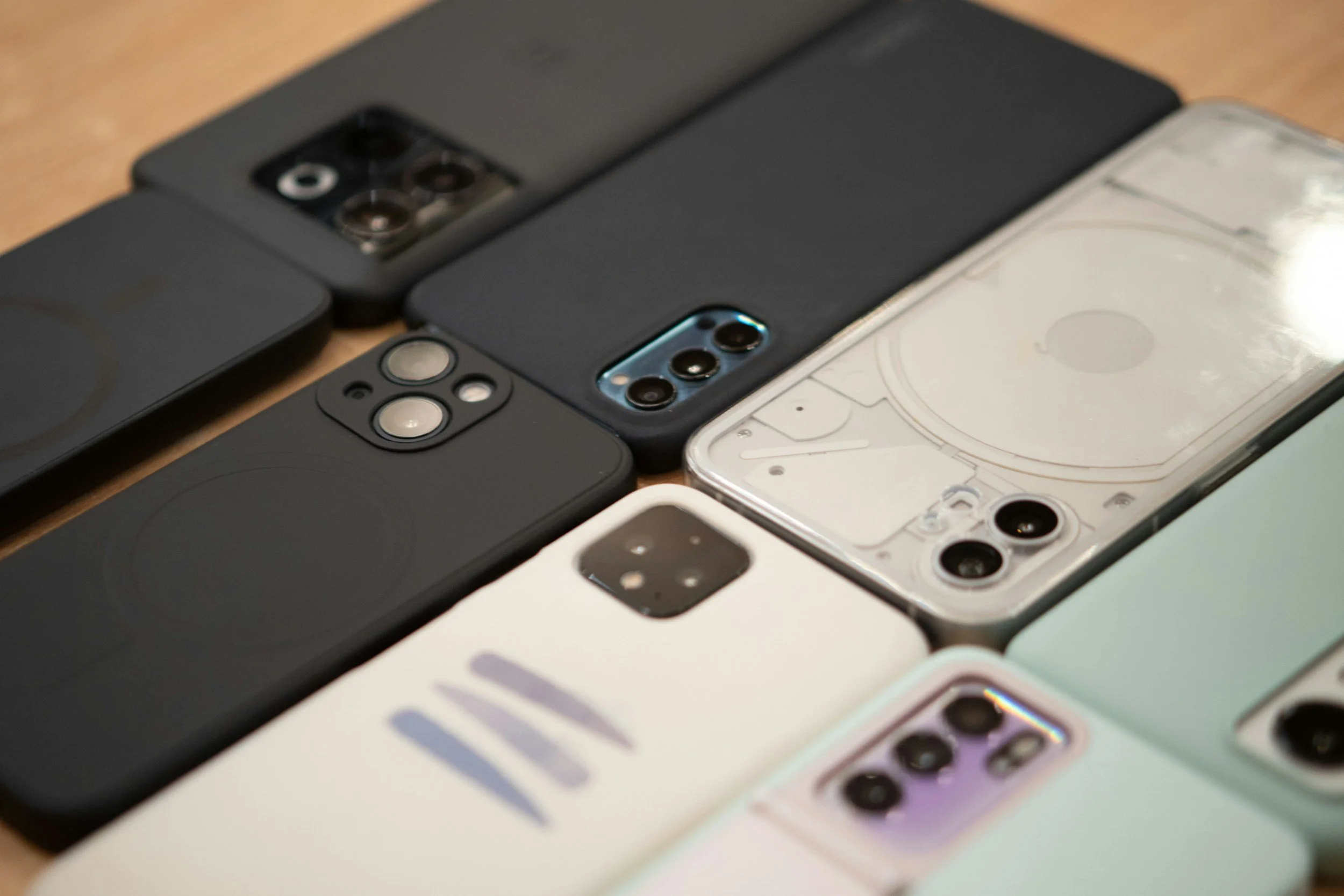 Multiple smartphones lined up on a wooden surface, showing different camera designs and colors.