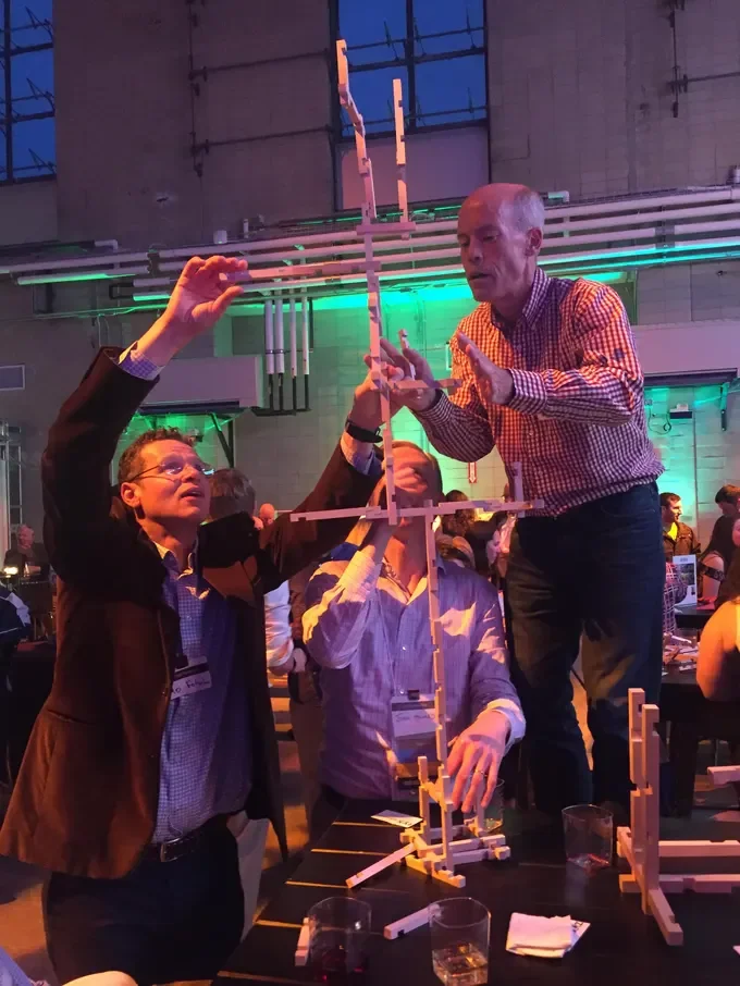 Three men wearing button down shirts building a tower using wooden ZYX Sticks