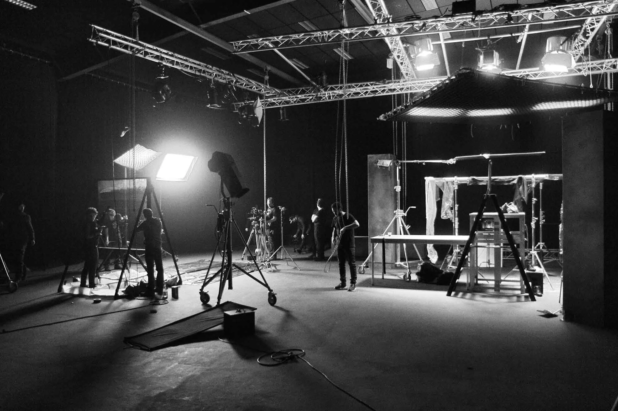 Black and white photo of a television or film studio with crew members setting up lighting and equipment.