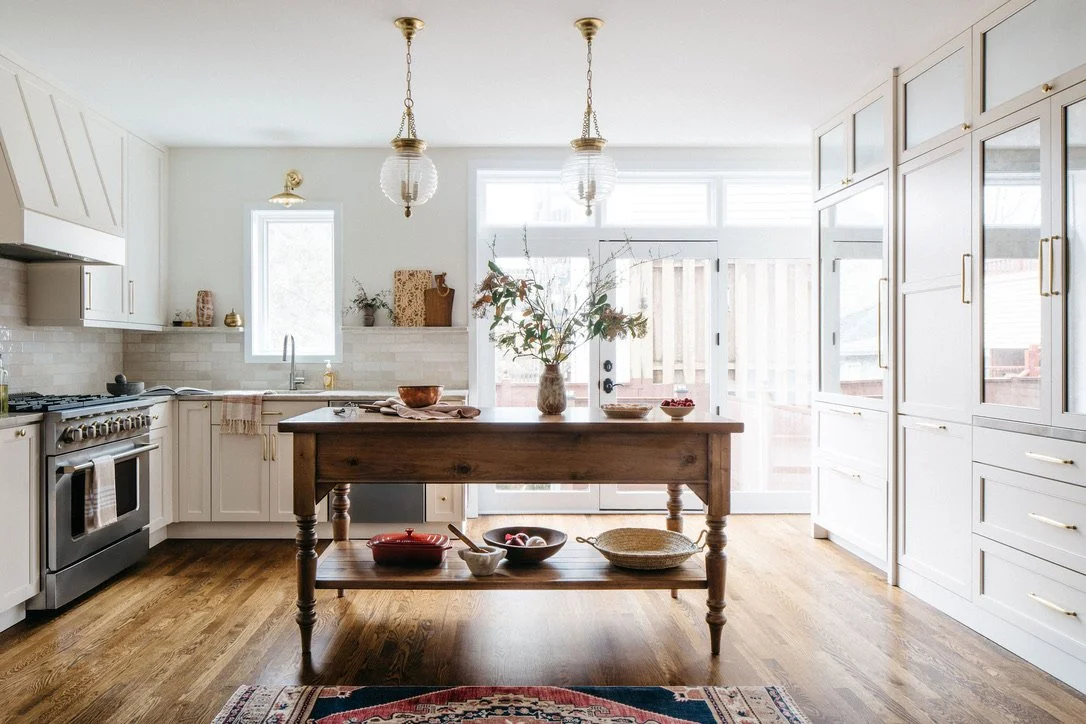 Bright kitchen with white cabinets, wooden island, hardwood floors, and large windowed doors with a floral arrangement on the island.