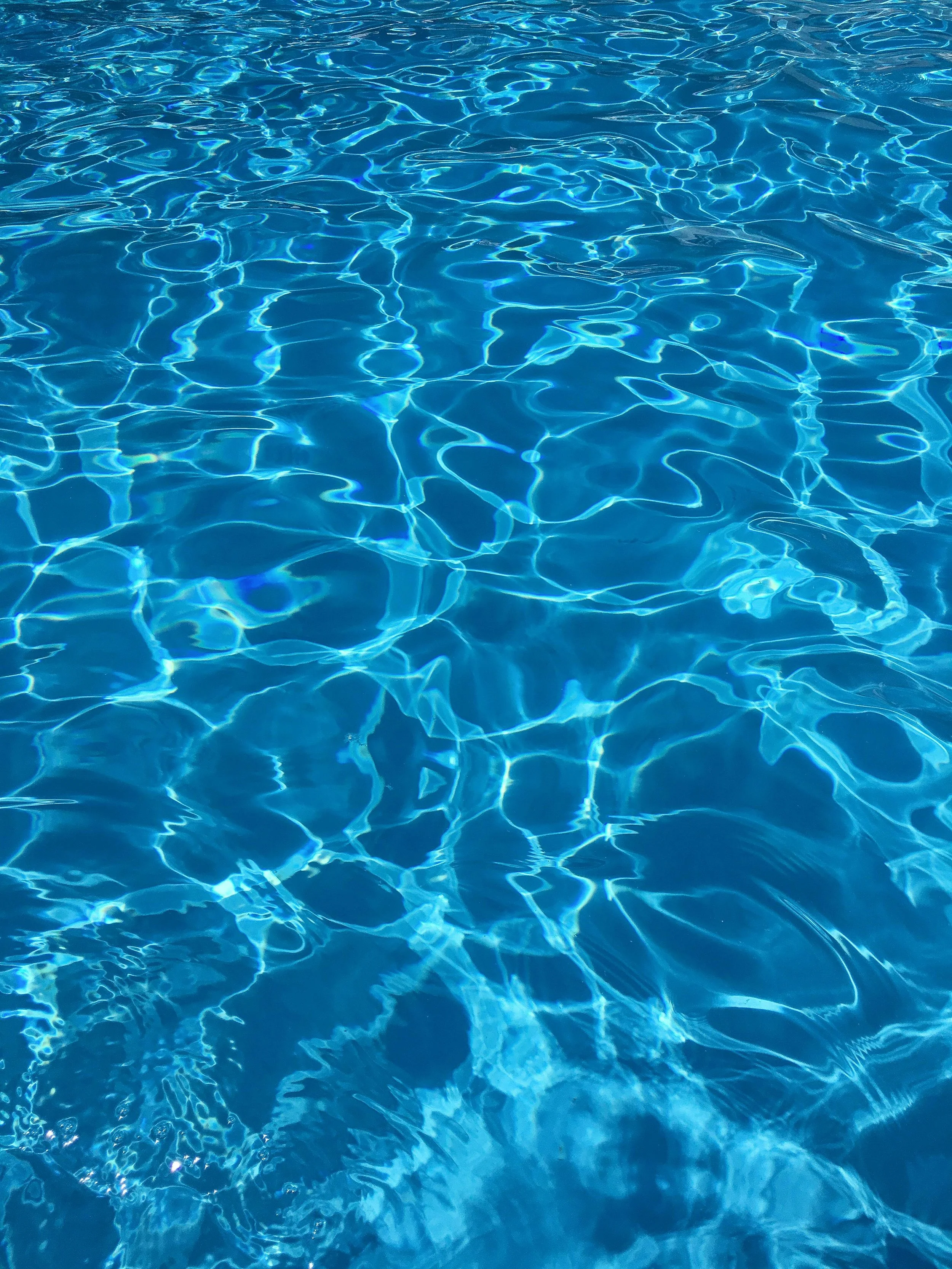 The image shows a close-up view of a swimming pool's water surface with sunlight creating reflections and ripples.
