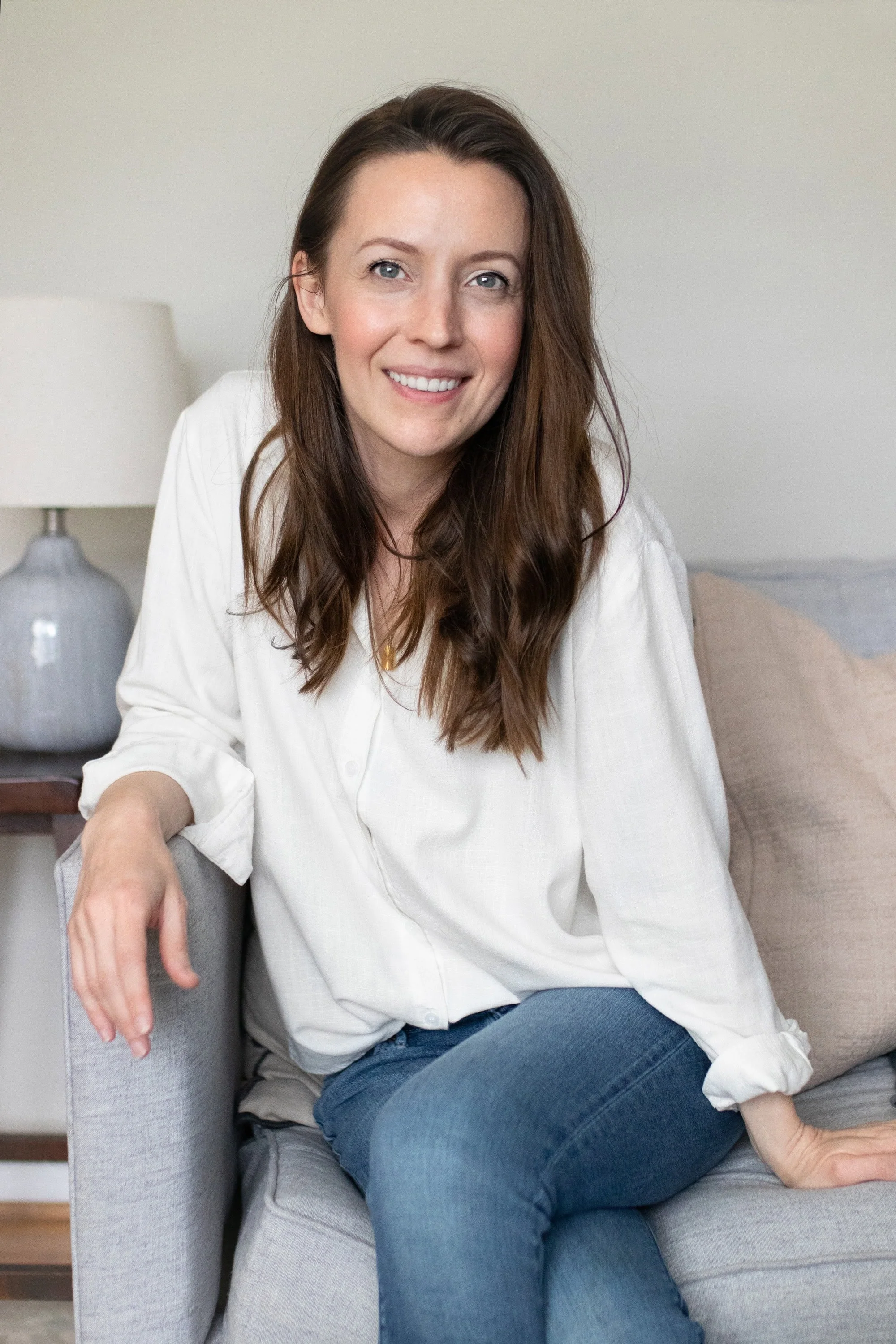 Steph Pollard sitting on a gray sofa smiling at the camera